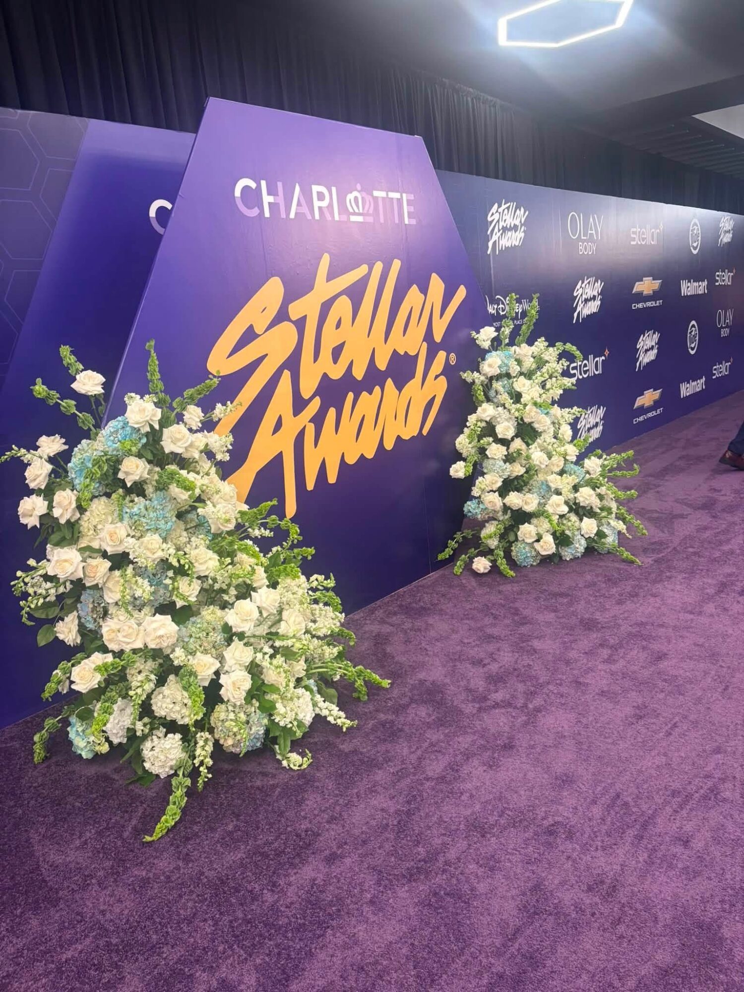 Purple backdrop with text 'Charlotte Star Award' and floral arrangements on purple carpet.