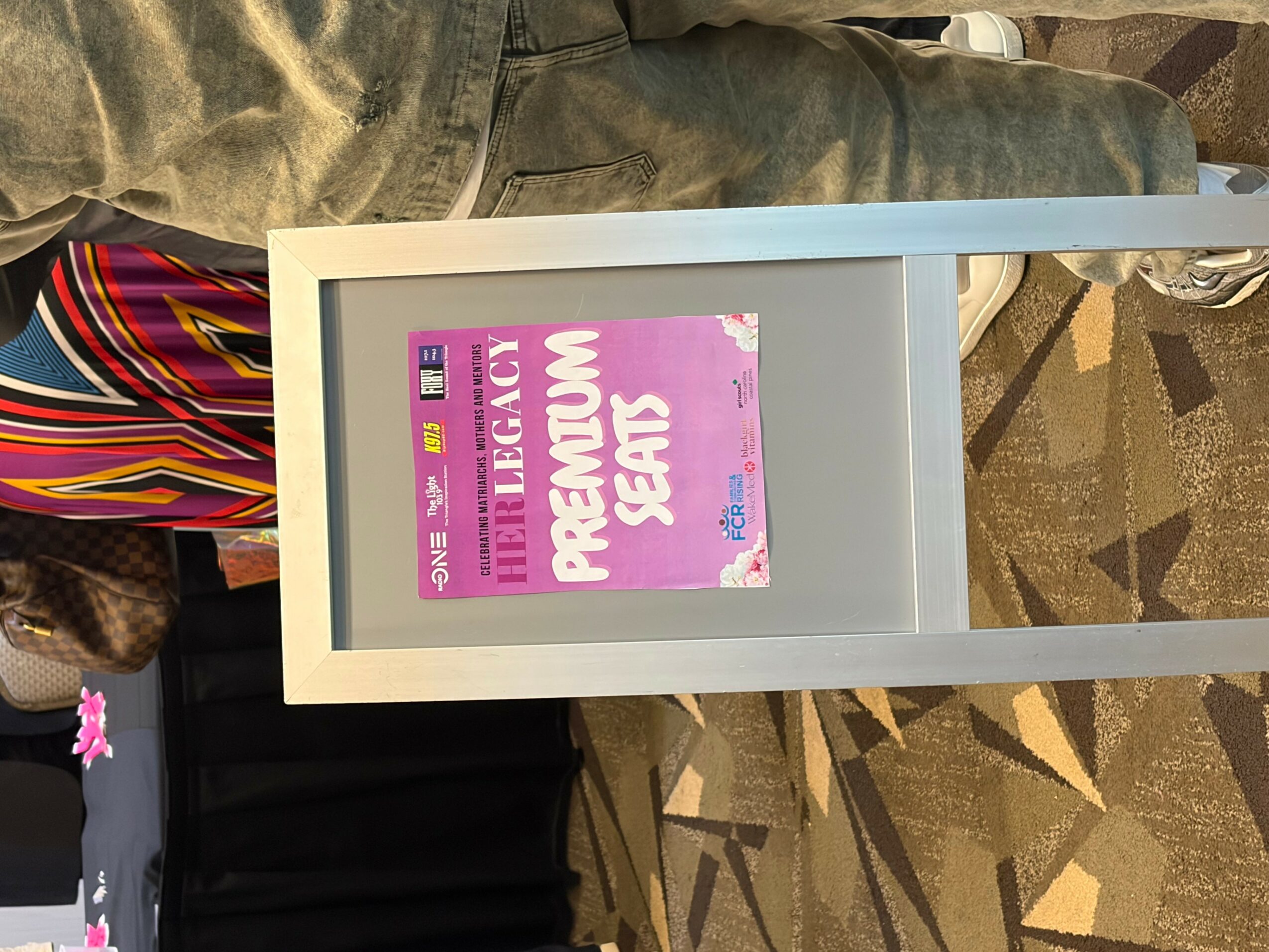 A white frame with a pink and purple poster inside, partially visible, on a patterned carpeted floor.