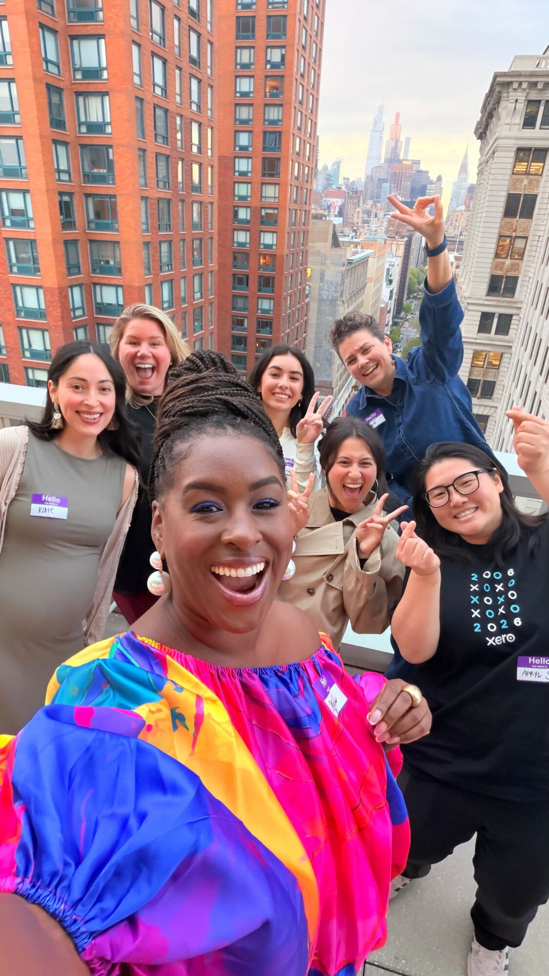 Group of seven diverse people smiling and celebrating on a rooftop with city buildings in the background.