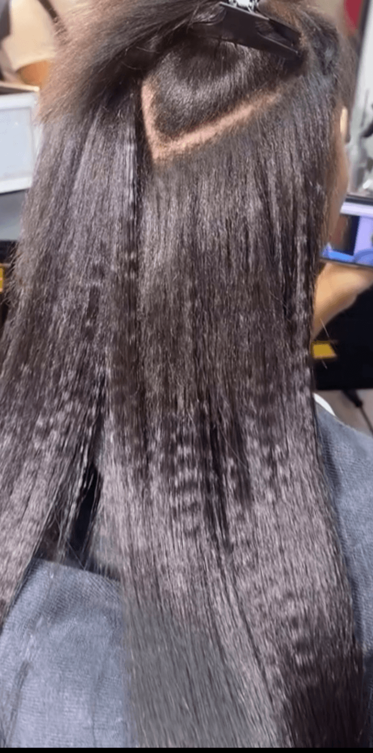 Person's hair with a section of straight, shiny hair and a visible scalp area, viewed from behind.