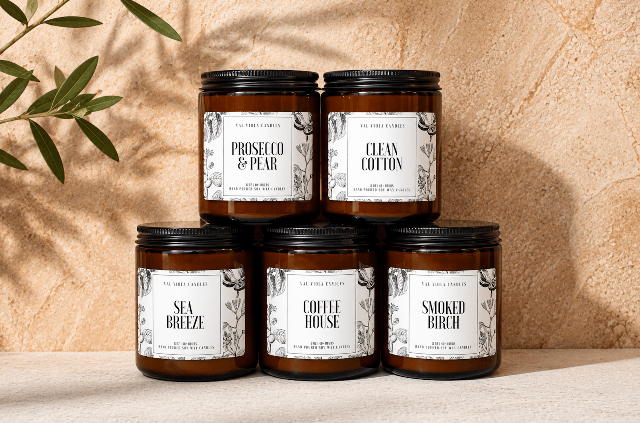 Five jars with white labels arranged on a surface against a textured beige background, with green leaves in the top left corner.