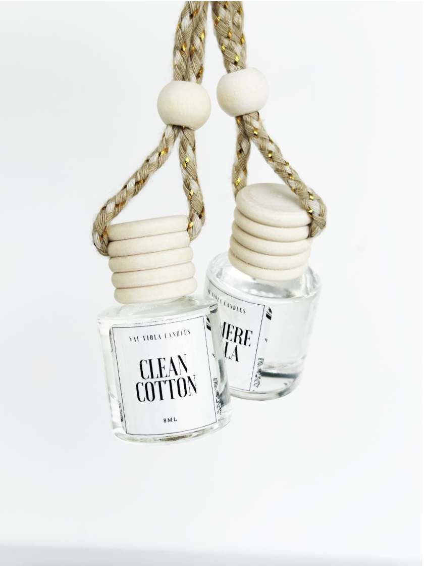 Two glass bottles with white labels hang by braided ropes with large white beads, against a white background.