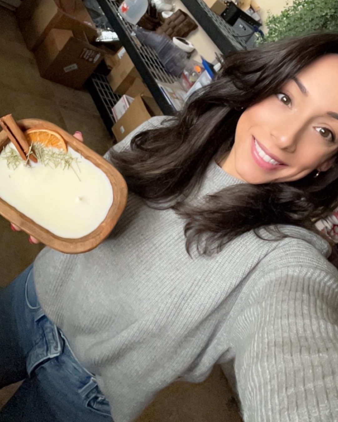 Woman smiling holding a wooden tray with a white substance, in a room with shelves and boxes