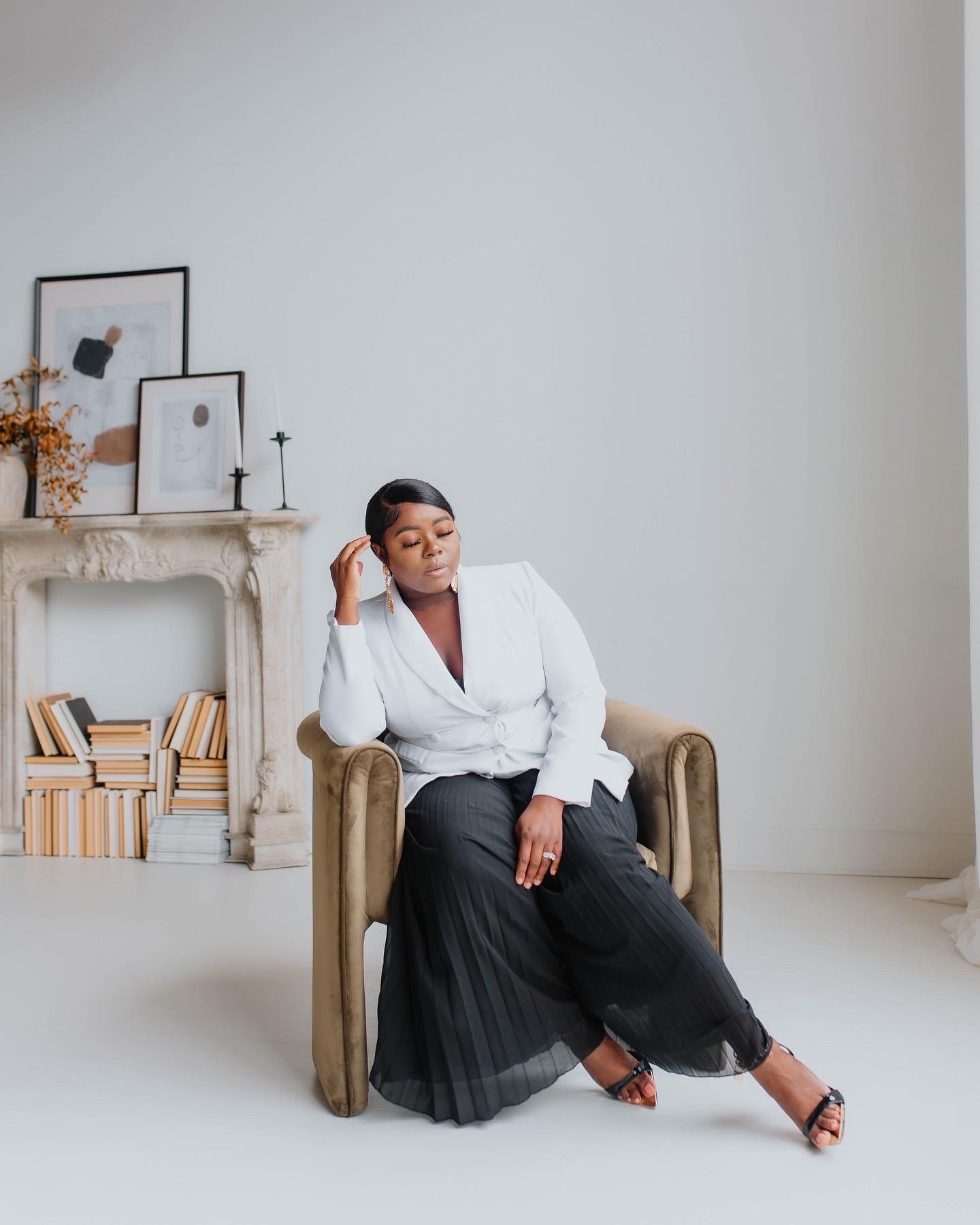Woman sitting in a chair in a minimalistic room with a fireplace and framed pictures on the wall.