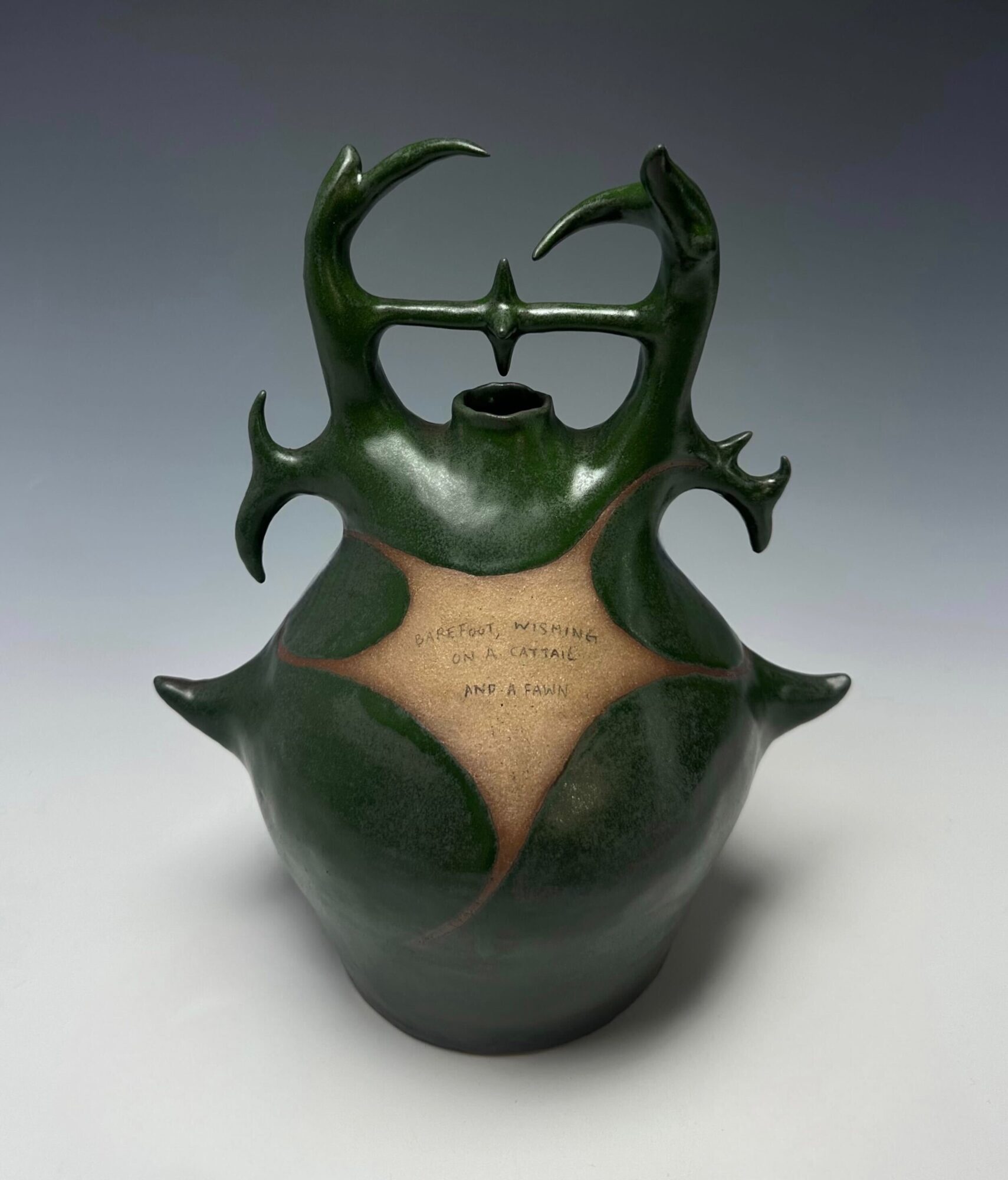 Green ceramic vessel with horn-like protrusions and a crack revealing a beige interior, set against a gray background.