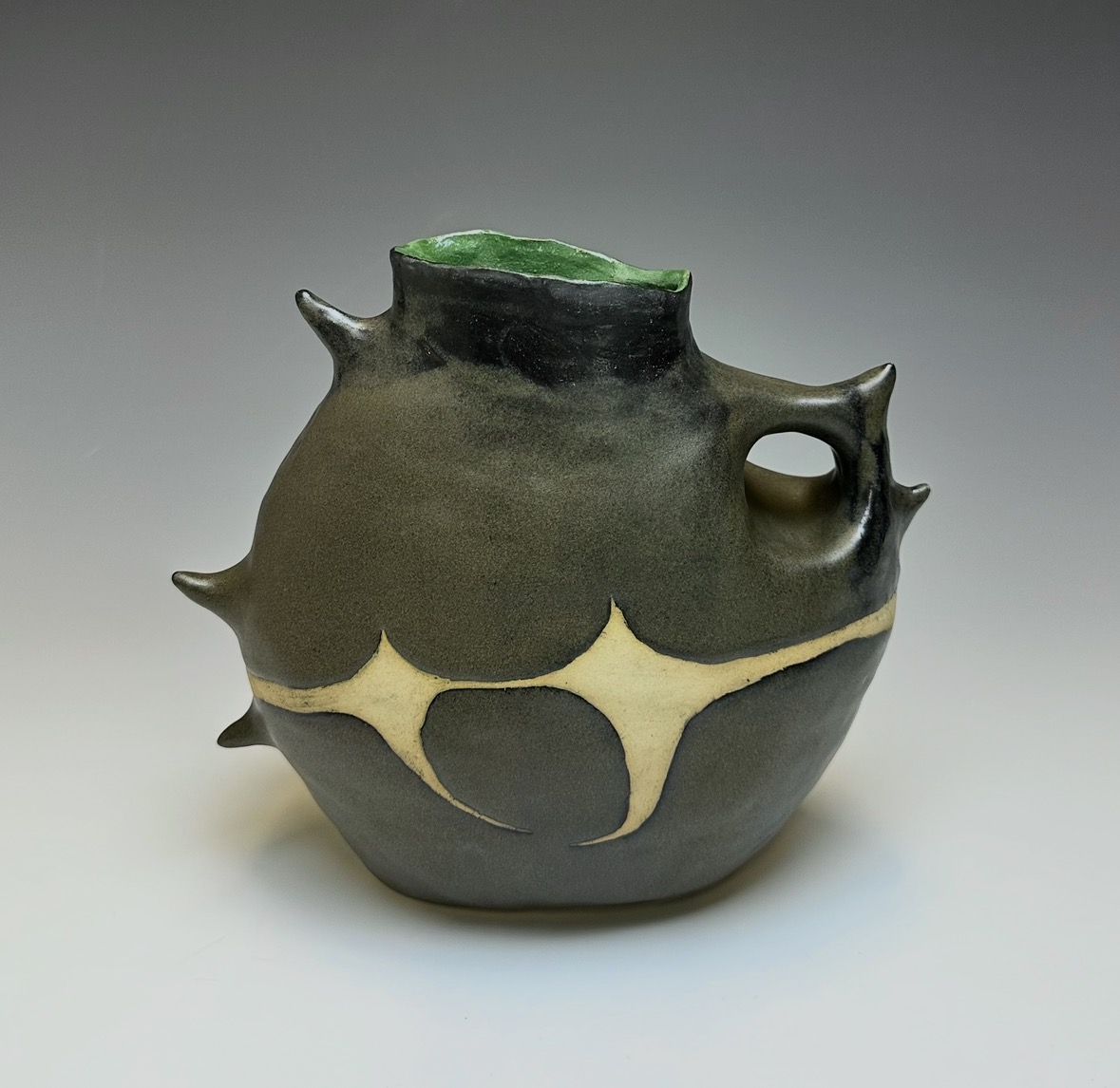 Ceramic vessel with a rounded body, spiked protrusions, and a small handle, featuring a black and cream color pattern.