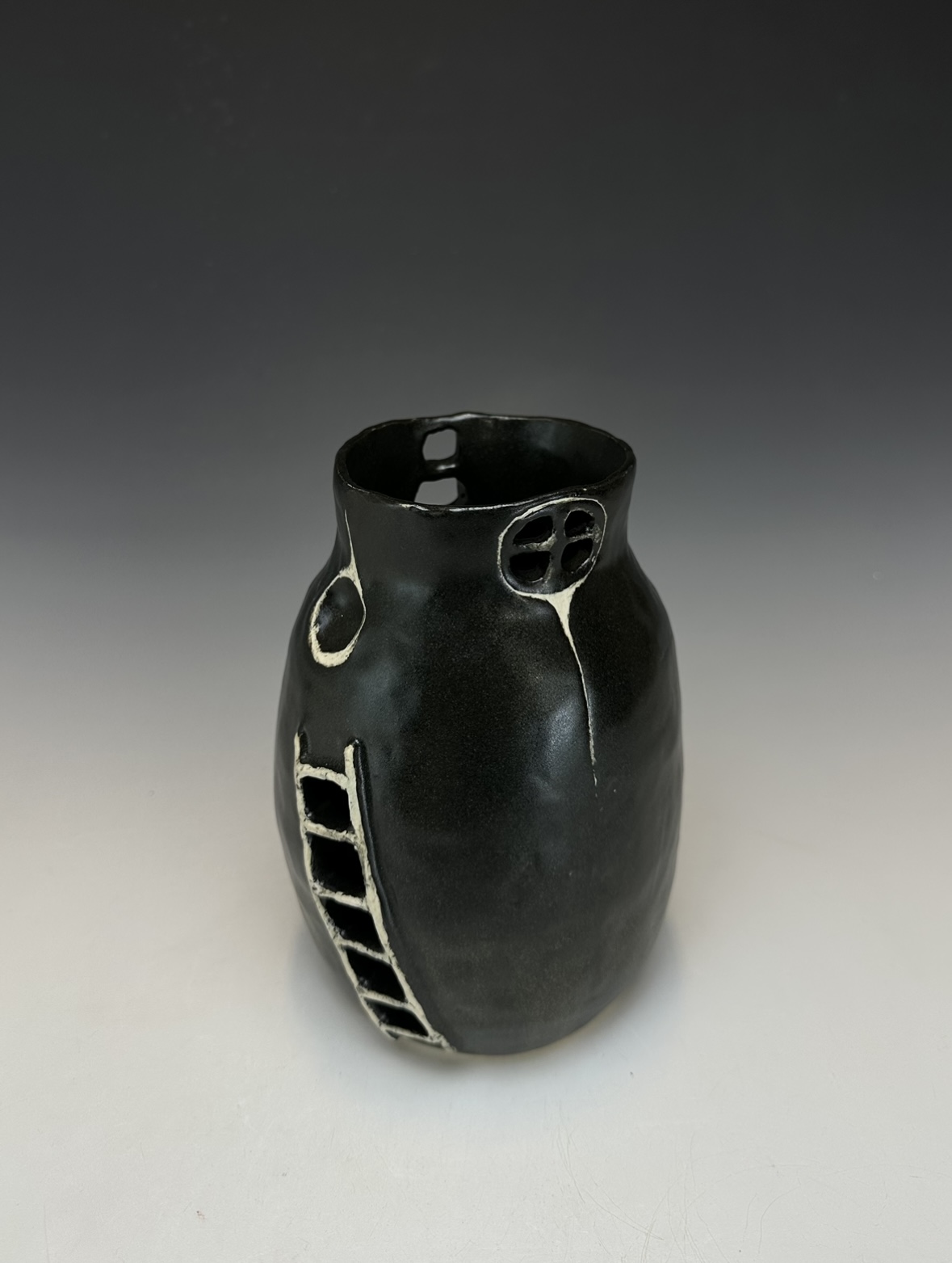 Black ceramic vase with circular and ladder-like decorative elements, set against a gradient background.