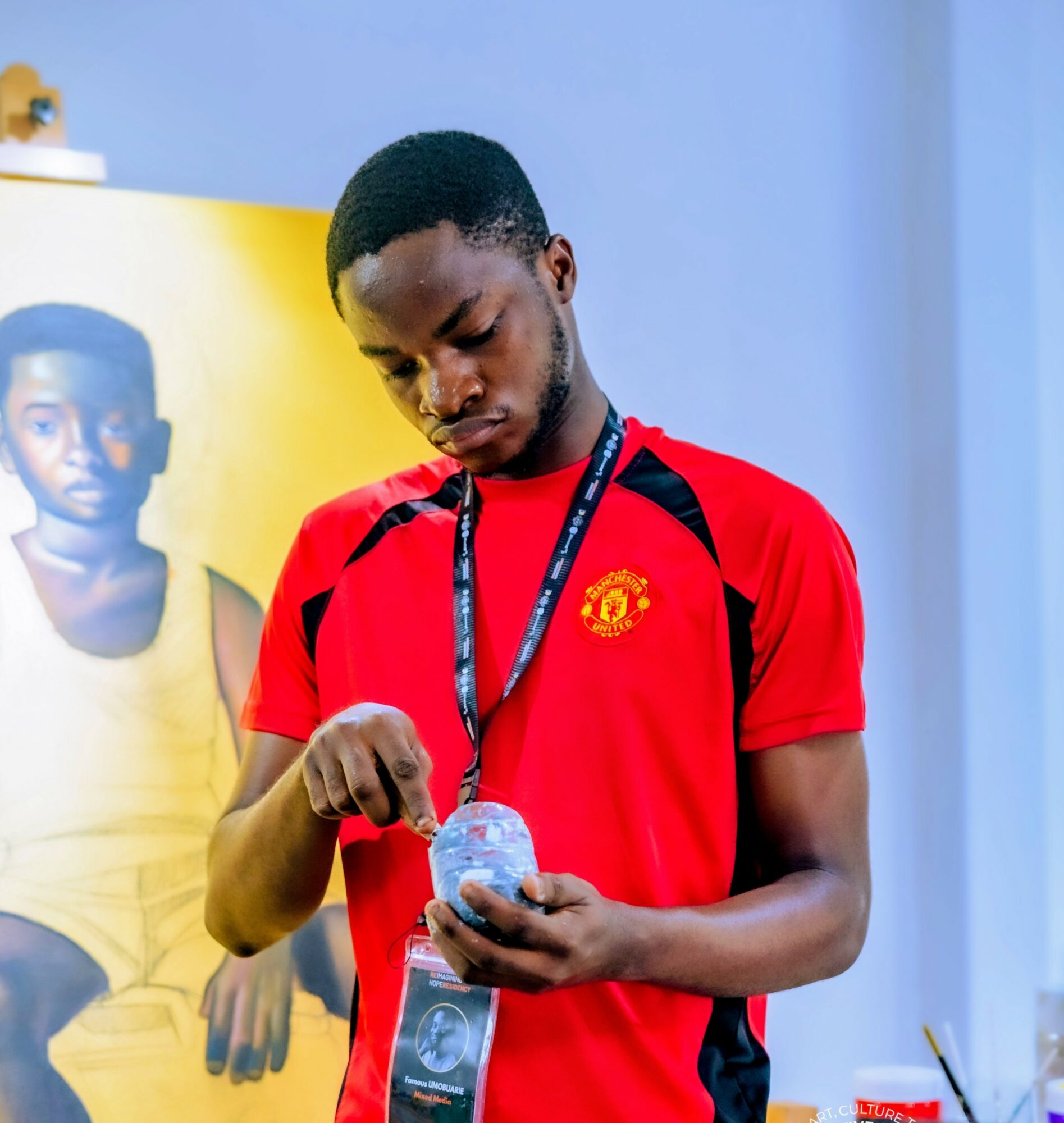 Young man in red shirt looking at a clear plastic water bottle, indoors with a yellow and blue background.
