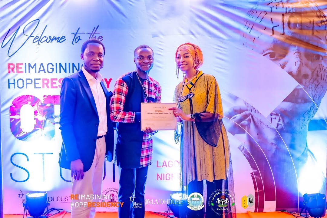 Three people standing on stage, one holding a certificate, with a colorful event backdrop behind them.