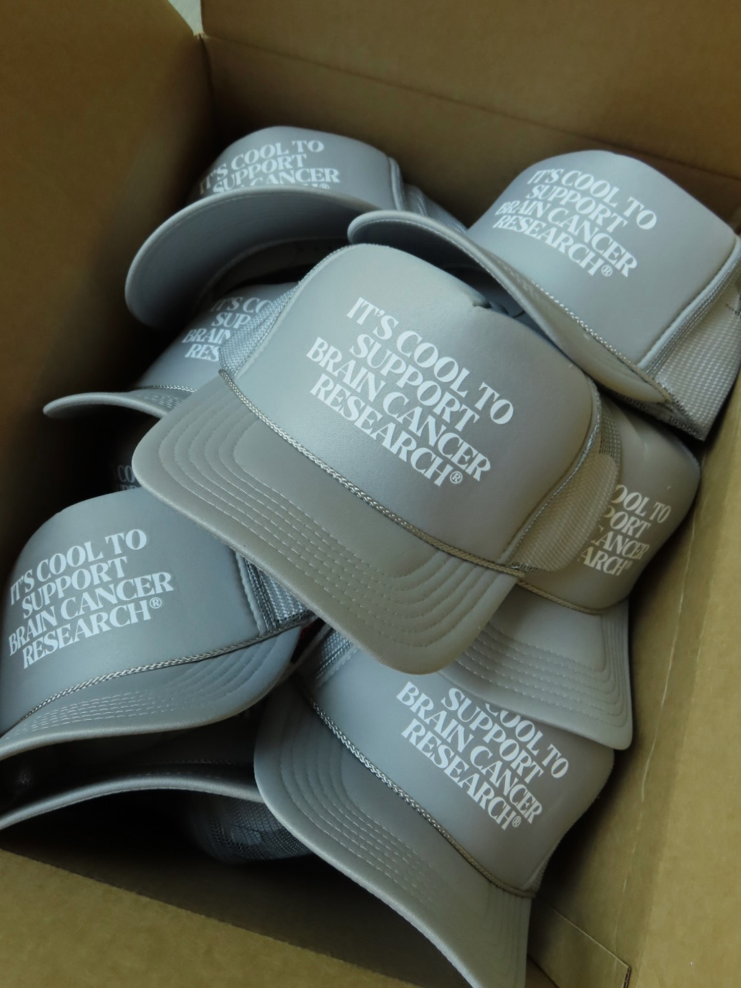 Gray caps with white text inside a cardboard box, some caps overlapping each other.