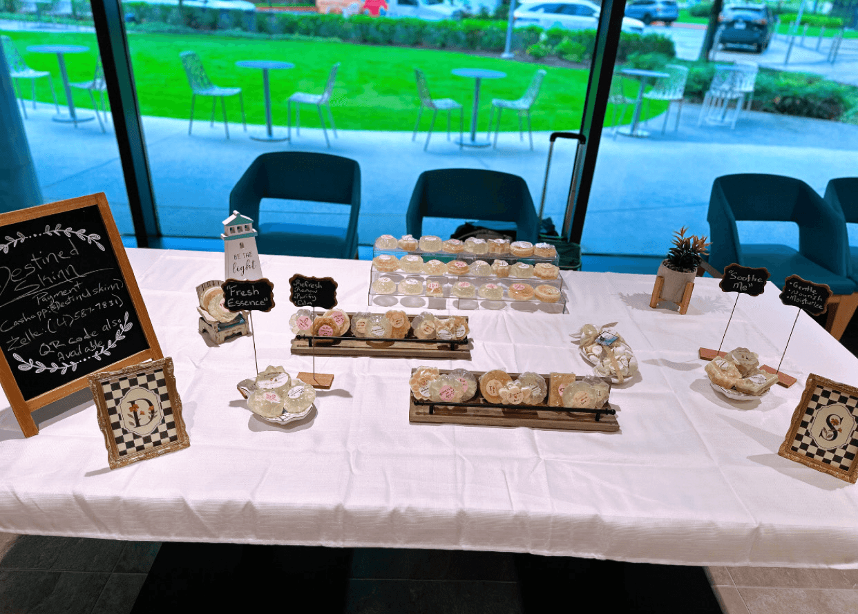 Table with desserts and chalkboard signs, set near large windows with outdoor view, chairs around the table.