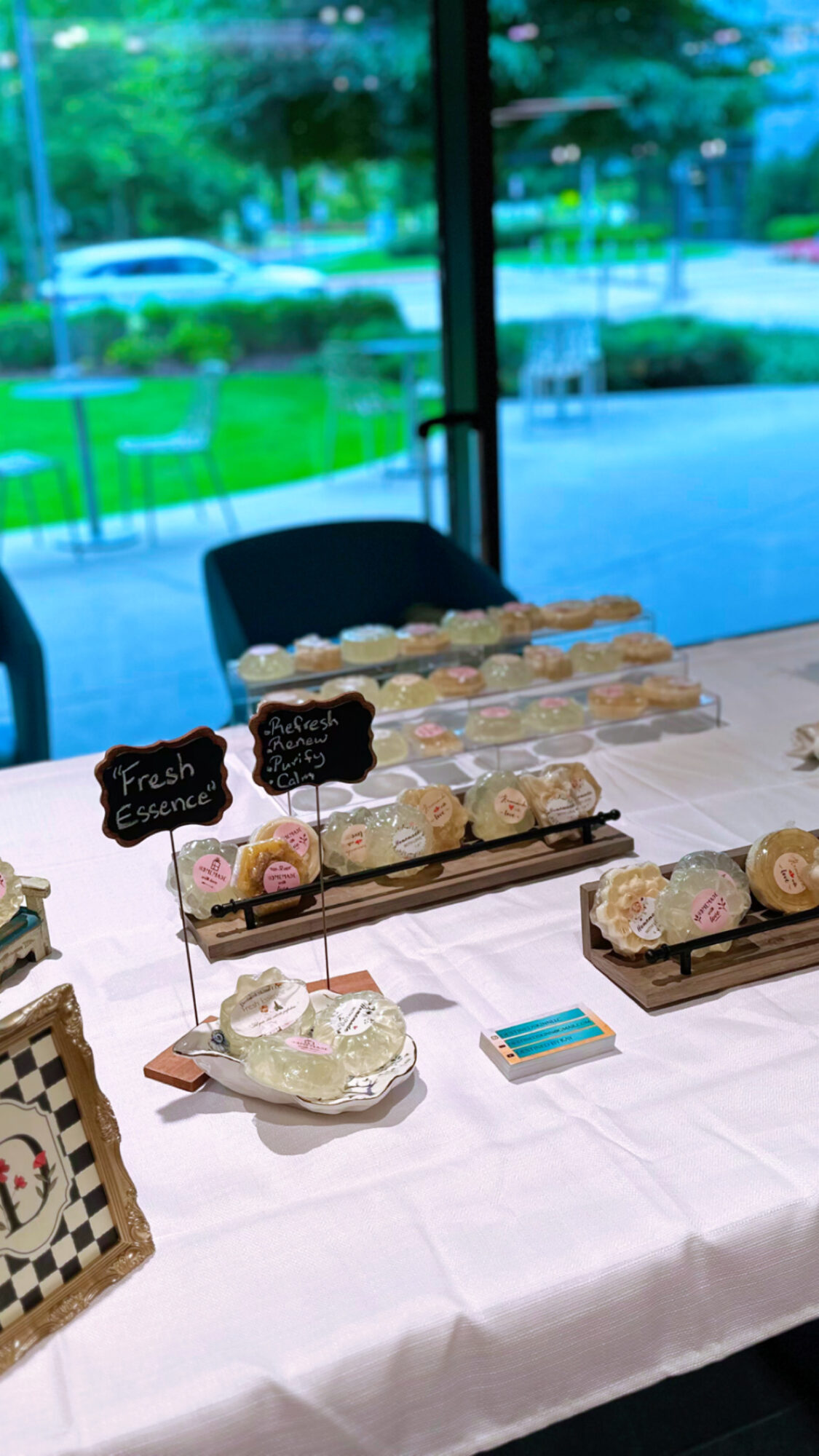 Table with decorated desserts and small chalkboard signs, set near large window with outdoor view.