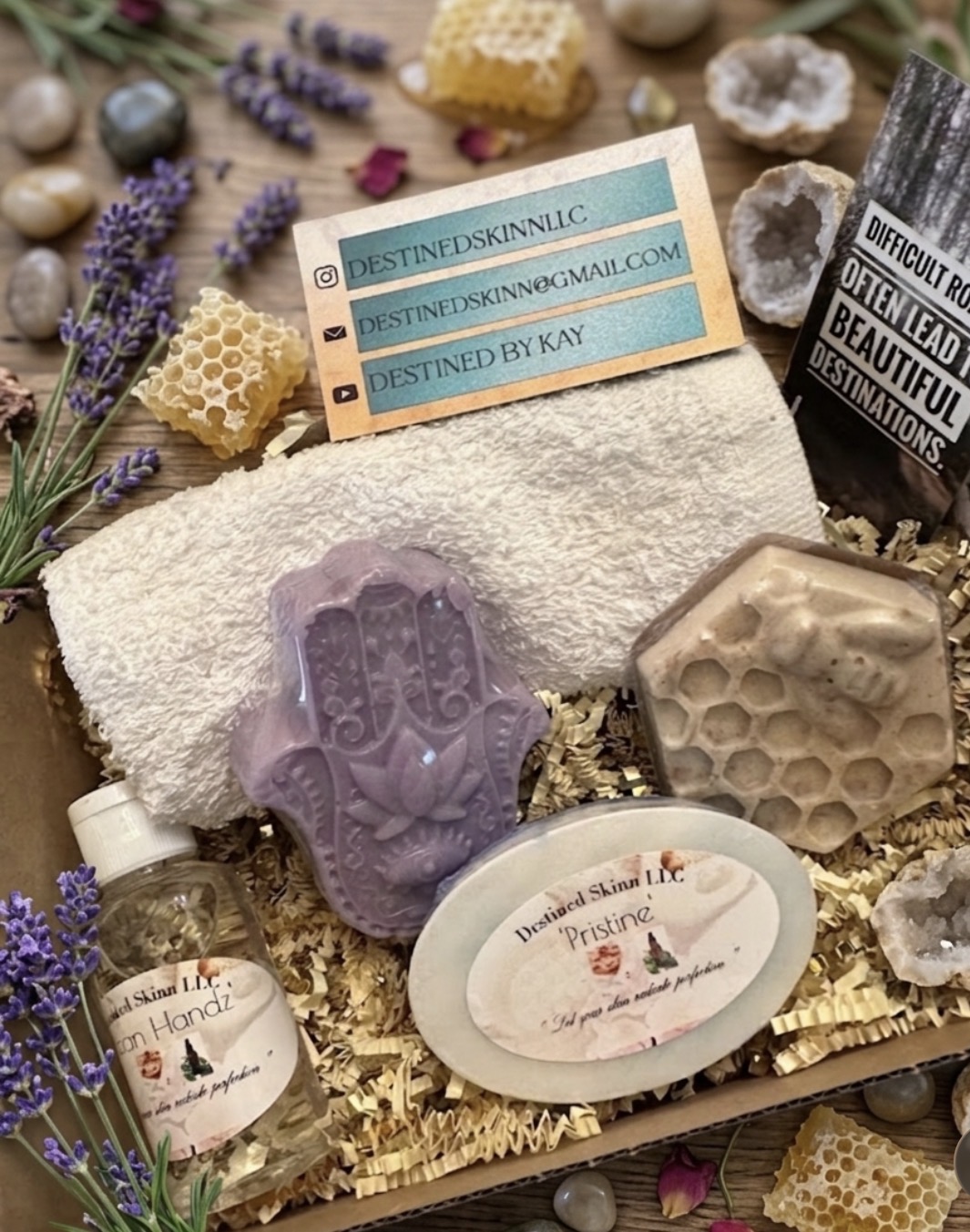 Spa and skincare products with lavender, honeycomb, and soap, arranged on a bed of shredded paper and surrounded by lavender flowers.