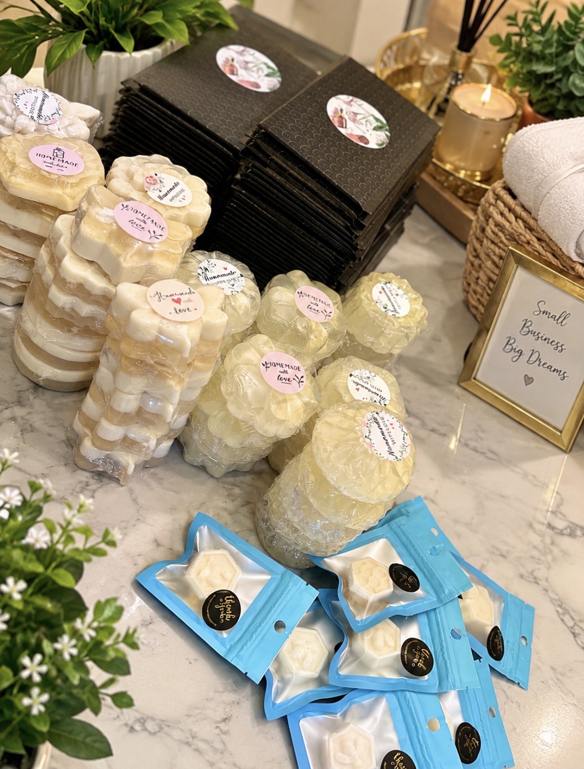 Stacked soap bars, black boxes, and small wrapped soap favors on a marble surface, with plants and decorative items nearby.