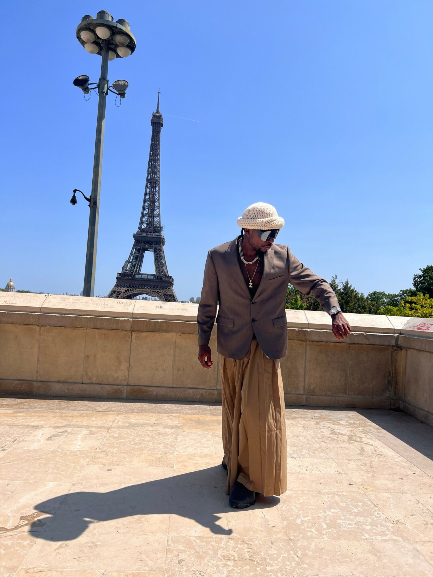 Person wearing a hat and coat standing on a concrete surface with a lamppost and clear blue sky in background.