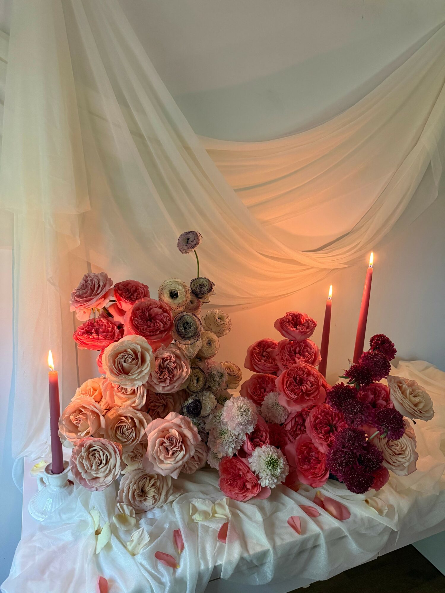 Bouquet of pink, red, and white roses with candles on a white fabric surface.