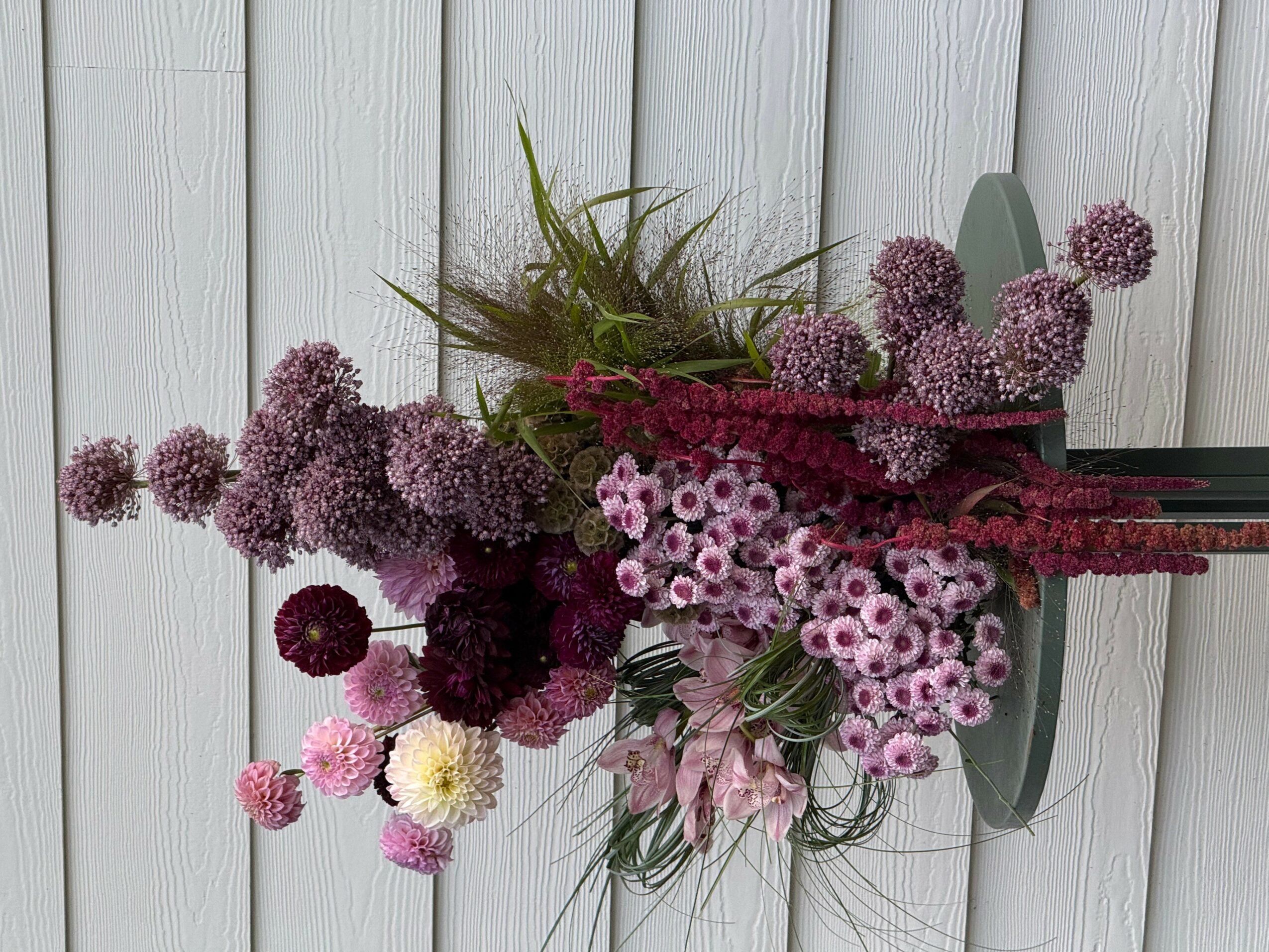 A bouquet of purple, pink, and white flowers with green foliage against a white wooden background.