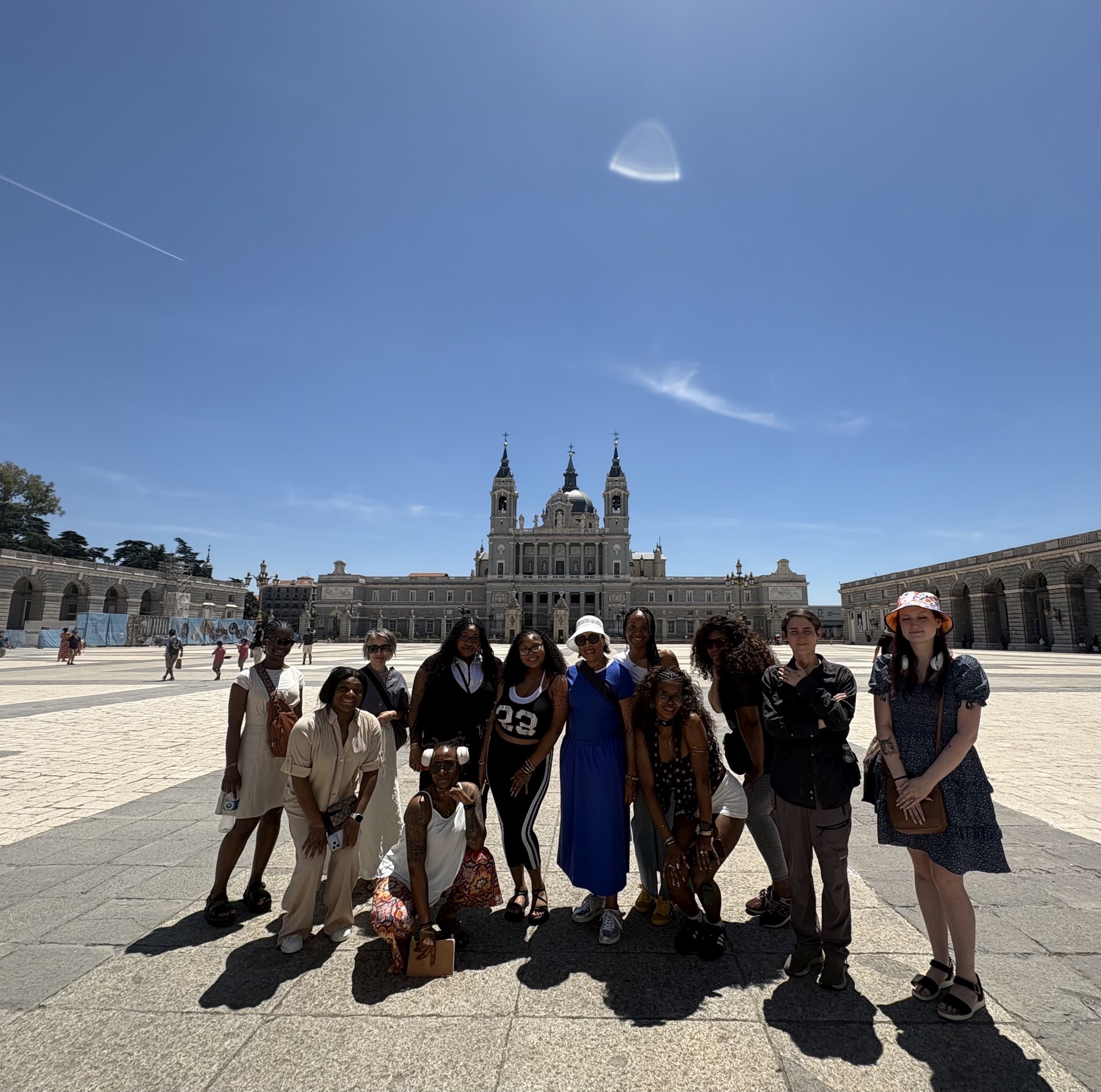 Group of people standing in front of a large historic building with towers, under a clear blue sky.
