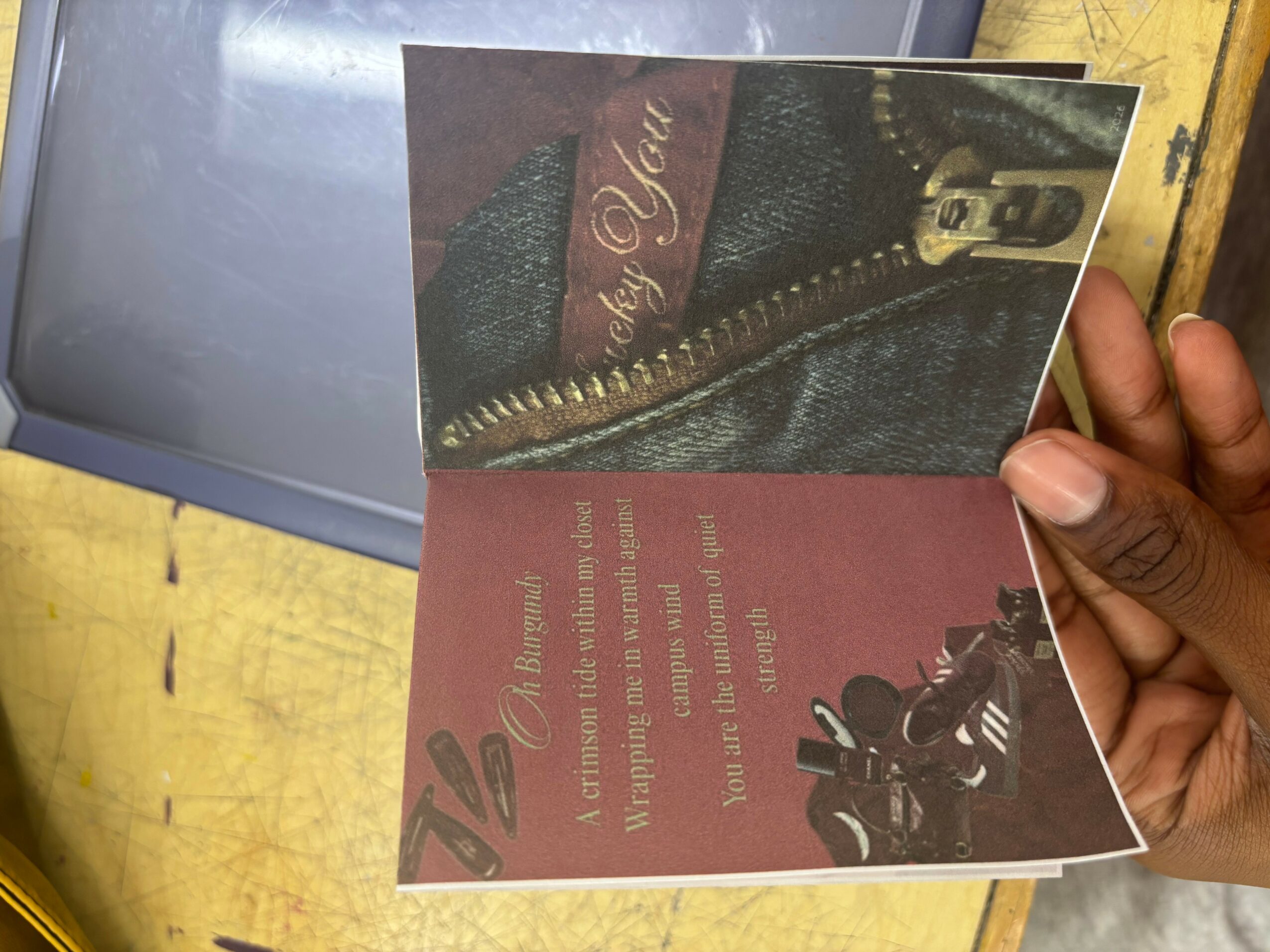A person holds a folded card with a red and black design, featuring a motorcycle and text, against a yellow surface.