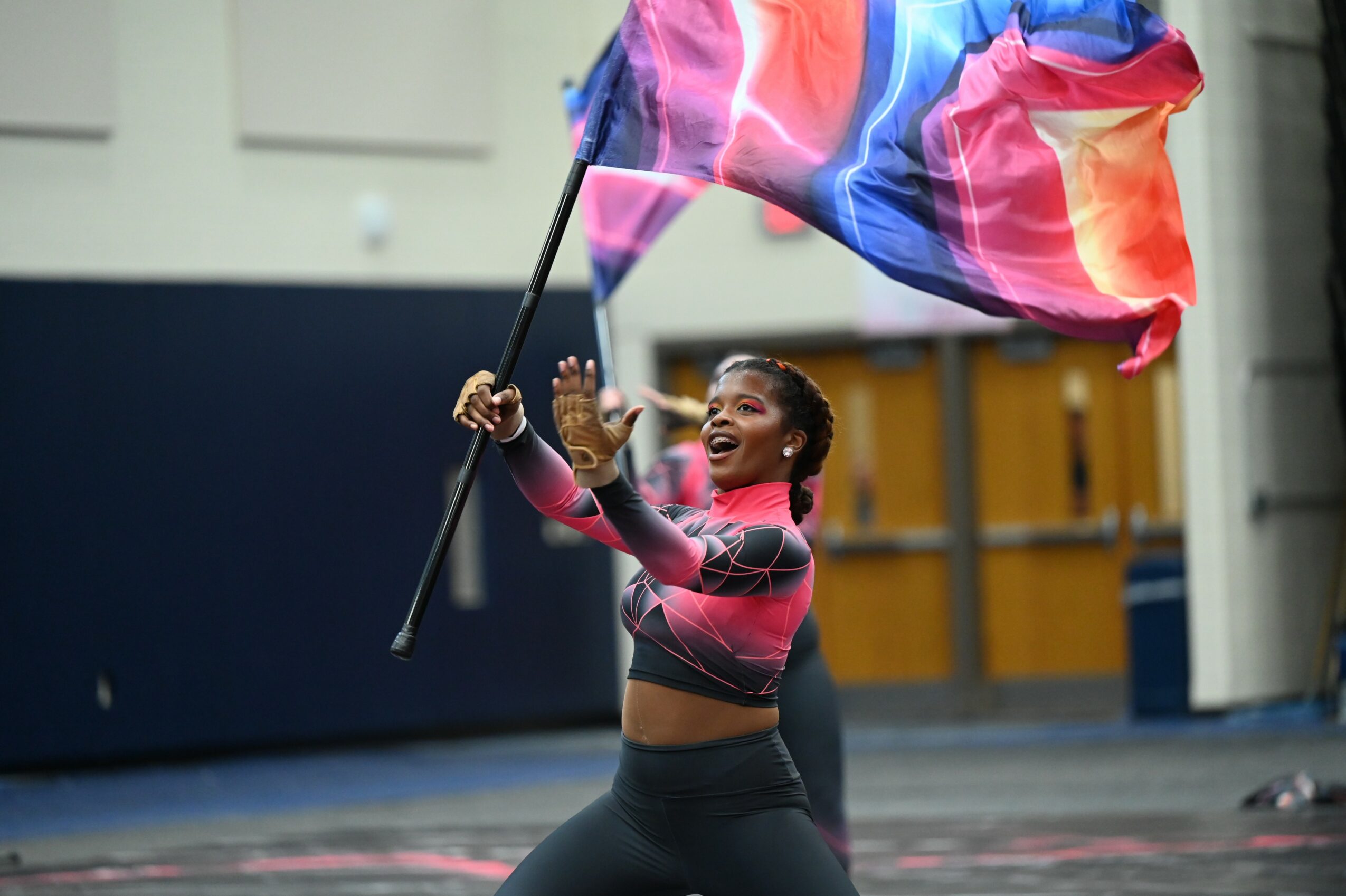 Young woman waving a large colorful flag indoors, smiling and celebrating, wearing a pink and black sports outfit.