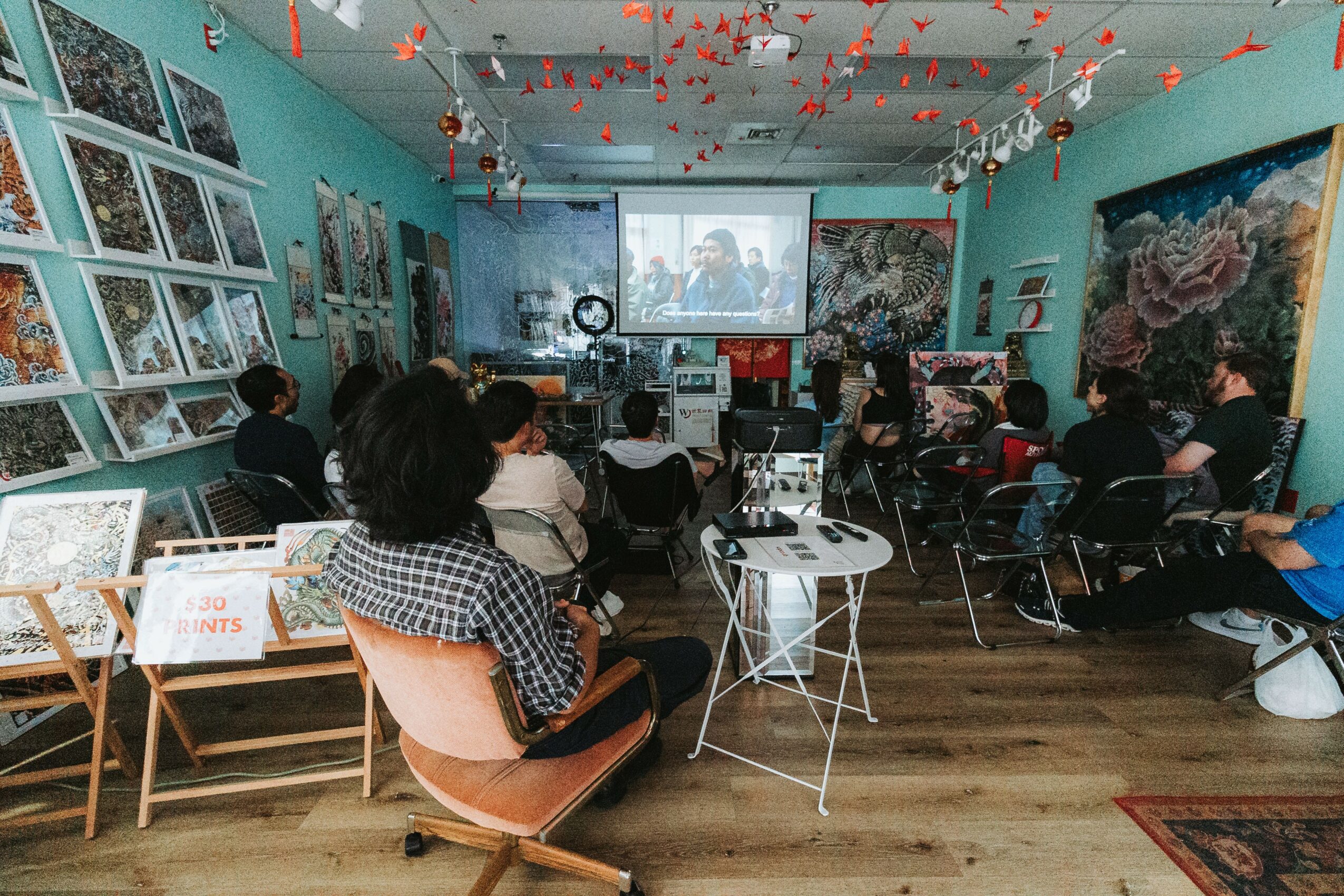 People watching a presentation or movie in a decorated room with artwork on walls and hanging decorations.