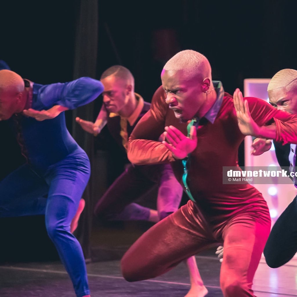 Group of performers in colorful costumes engaged in a dance or theatrical performance on stage.