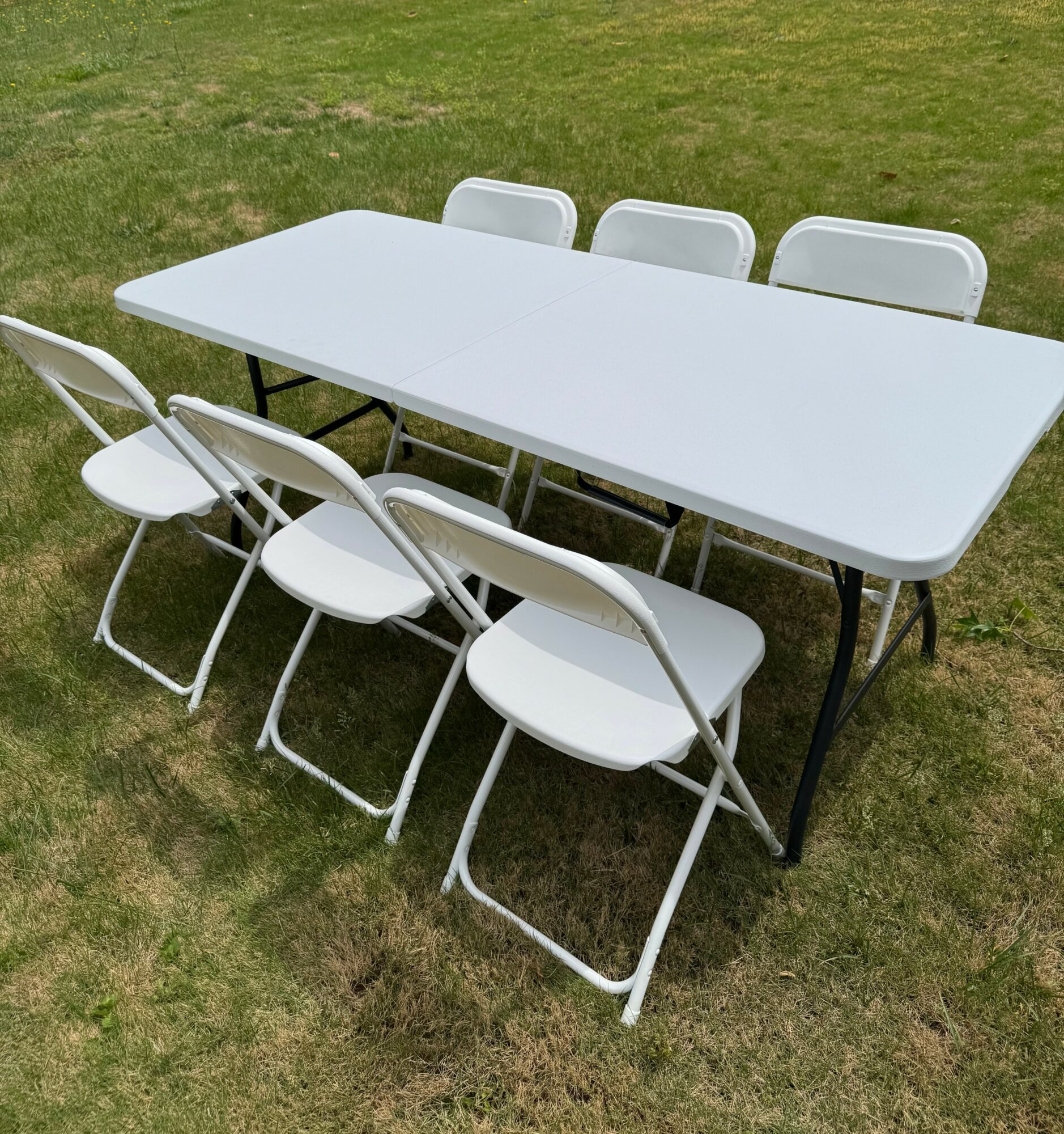 White outdoor table with six white chairs on grass, three chairs on each side, two at each end.