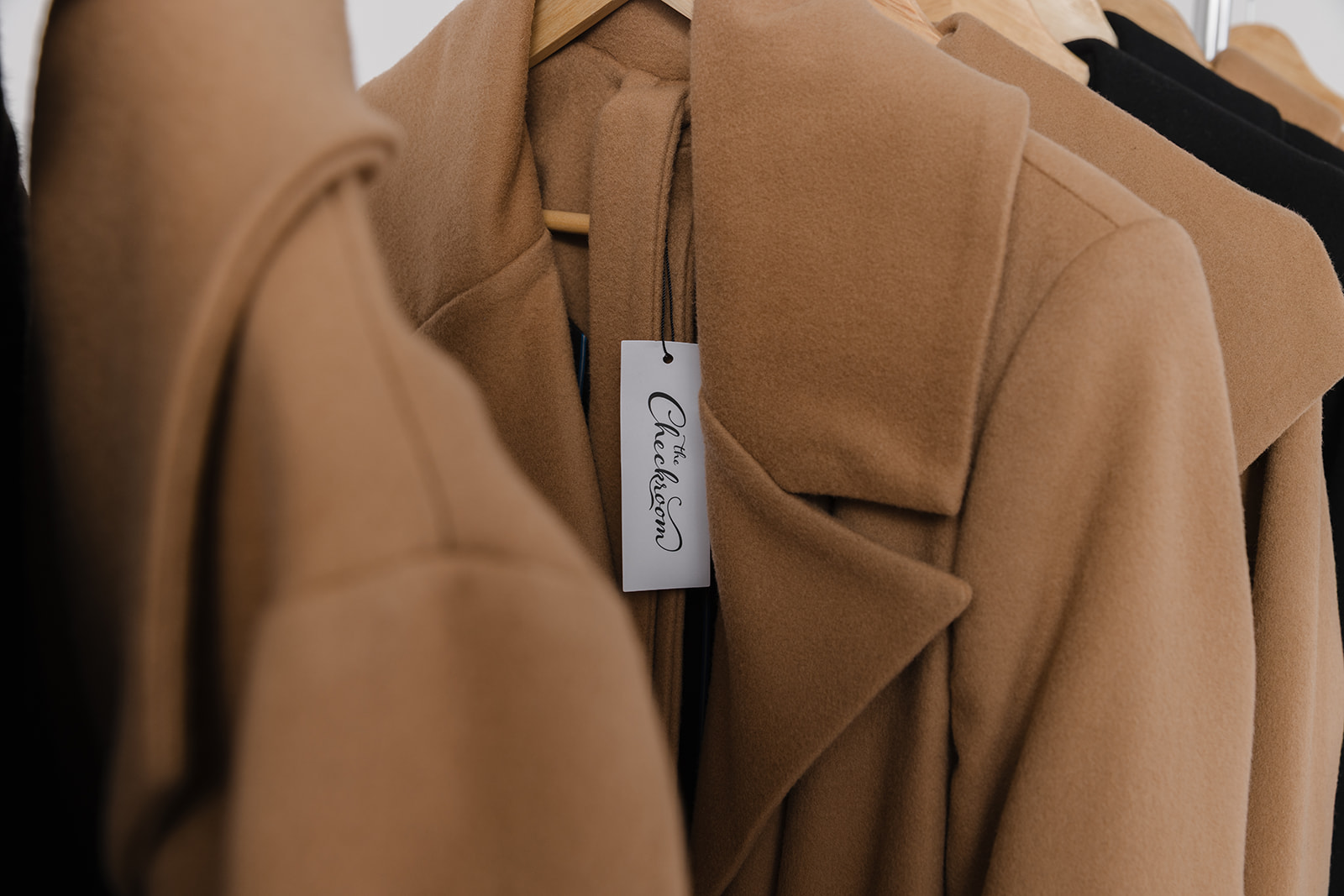 Close-up of beige coats hanging on a rack, showing tags and fabric details.