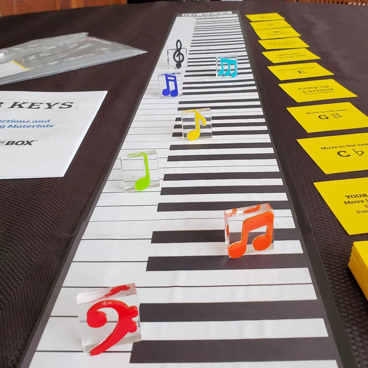Colorful musical notes and yellow cards arranged on a piano keyboard, with a sheet of paper on the side.
