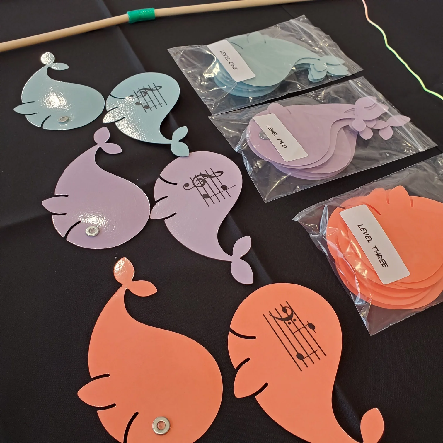 Colorful paper fish cutouts in pastel purple, blue, and orange, with some in plastic bags, on a black surface.