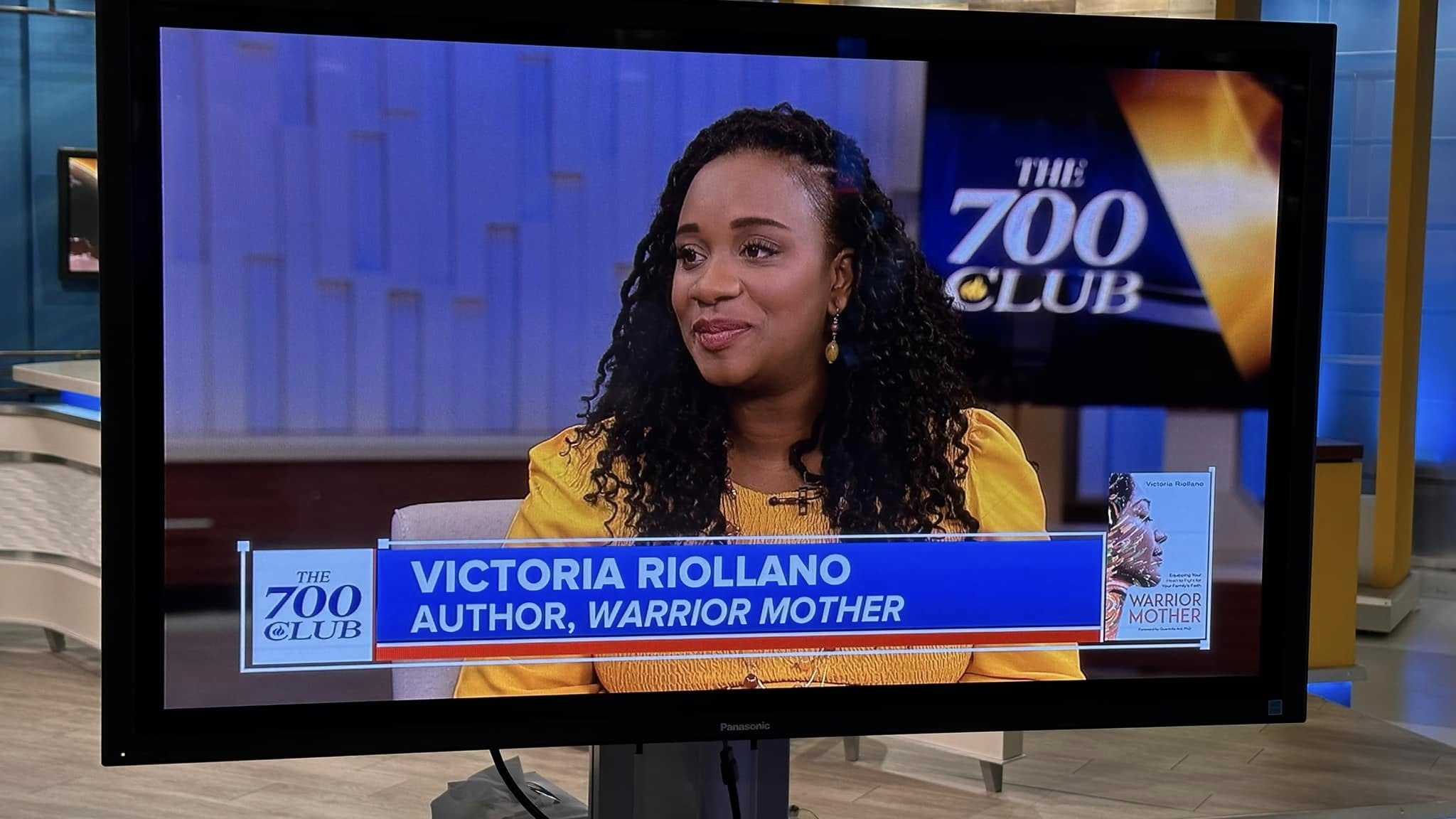 Woman with curly hair on TV screen, blue background, text overlay with name and book title, logo in corner.