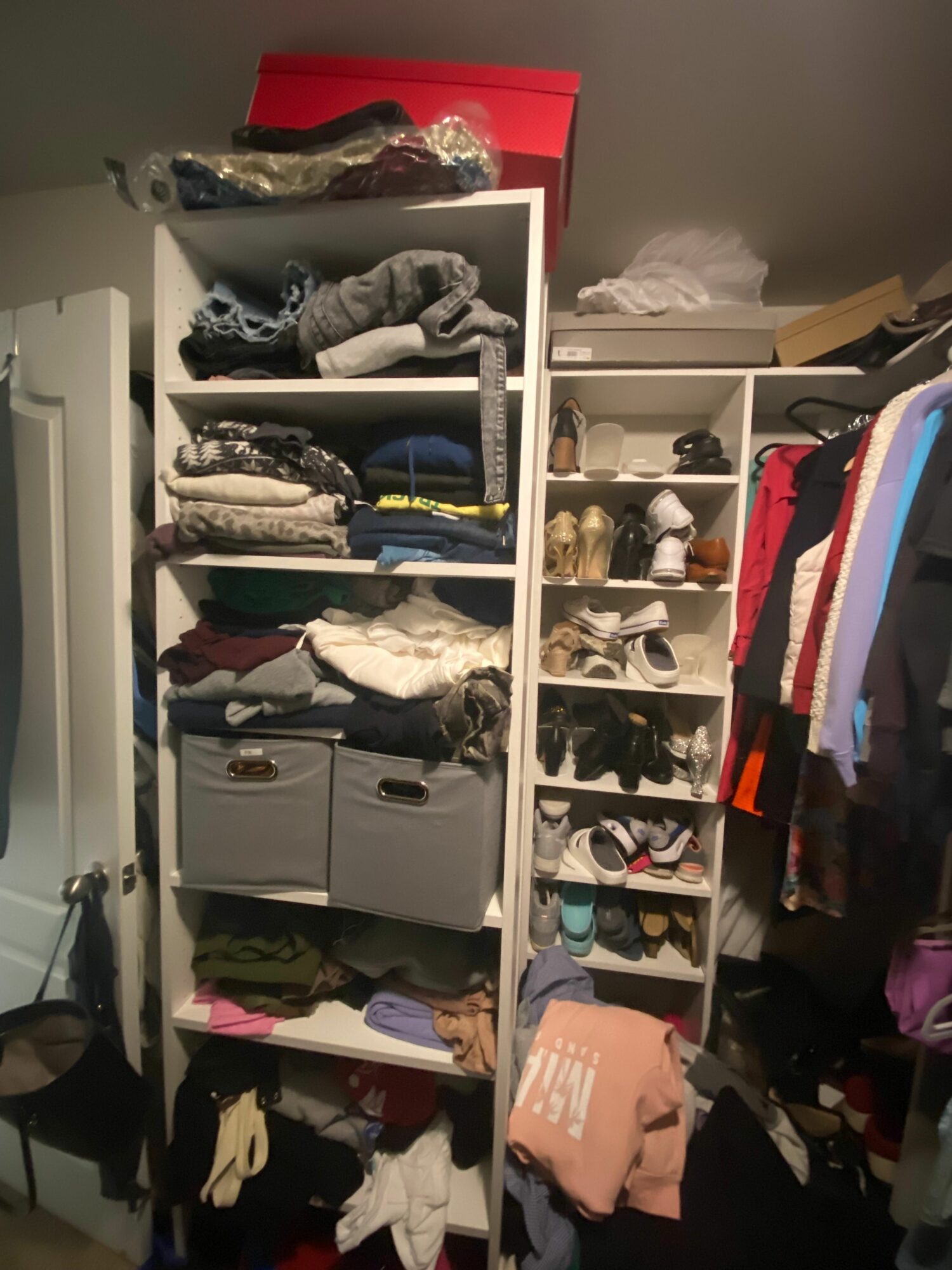 Closet with shelves filled with folded clothes, shoes, and storage boxes, with hanging clothes above and items on the floor.