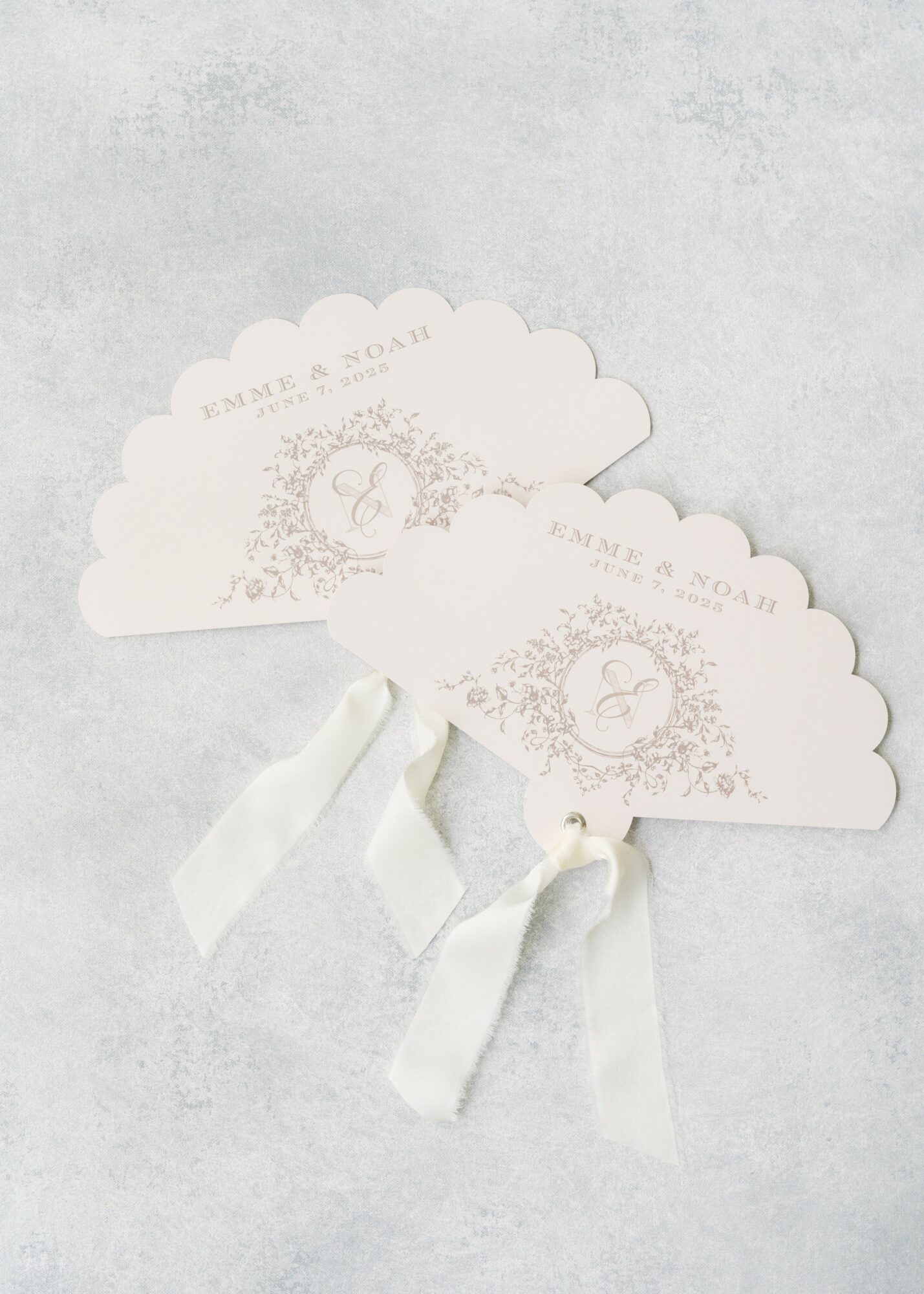 Two cloud-shaped paper fans with ribbons, decorated with floral and circular designs, placed on a light surface.
