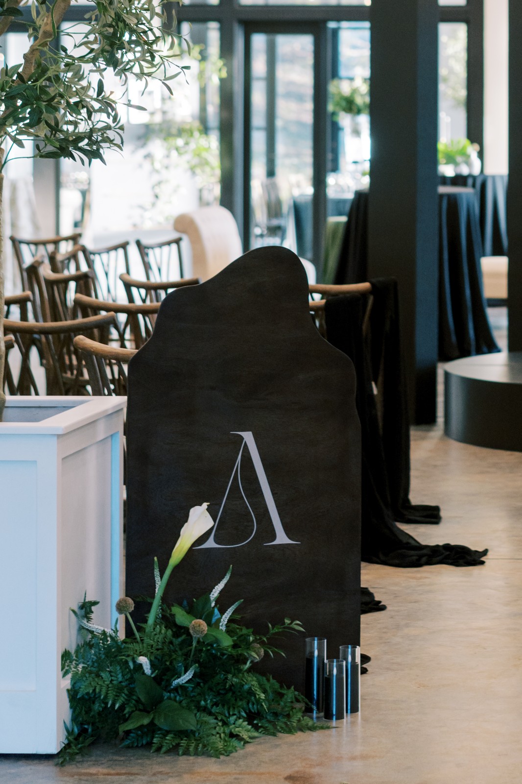 Chalkboard sign with a white letter A, surrounded by green plants, inside a well-lit indoor space with chairs and tables.