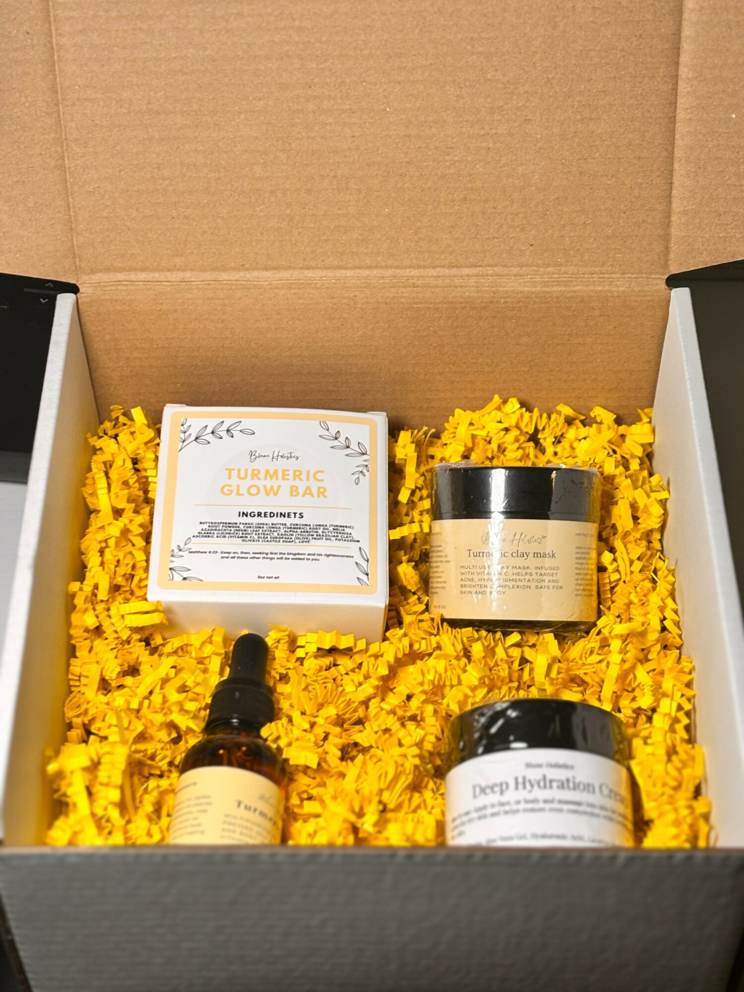 Open box containing skincare products on yellow shredded paper, including a box, two jars, and a dropper bottle.