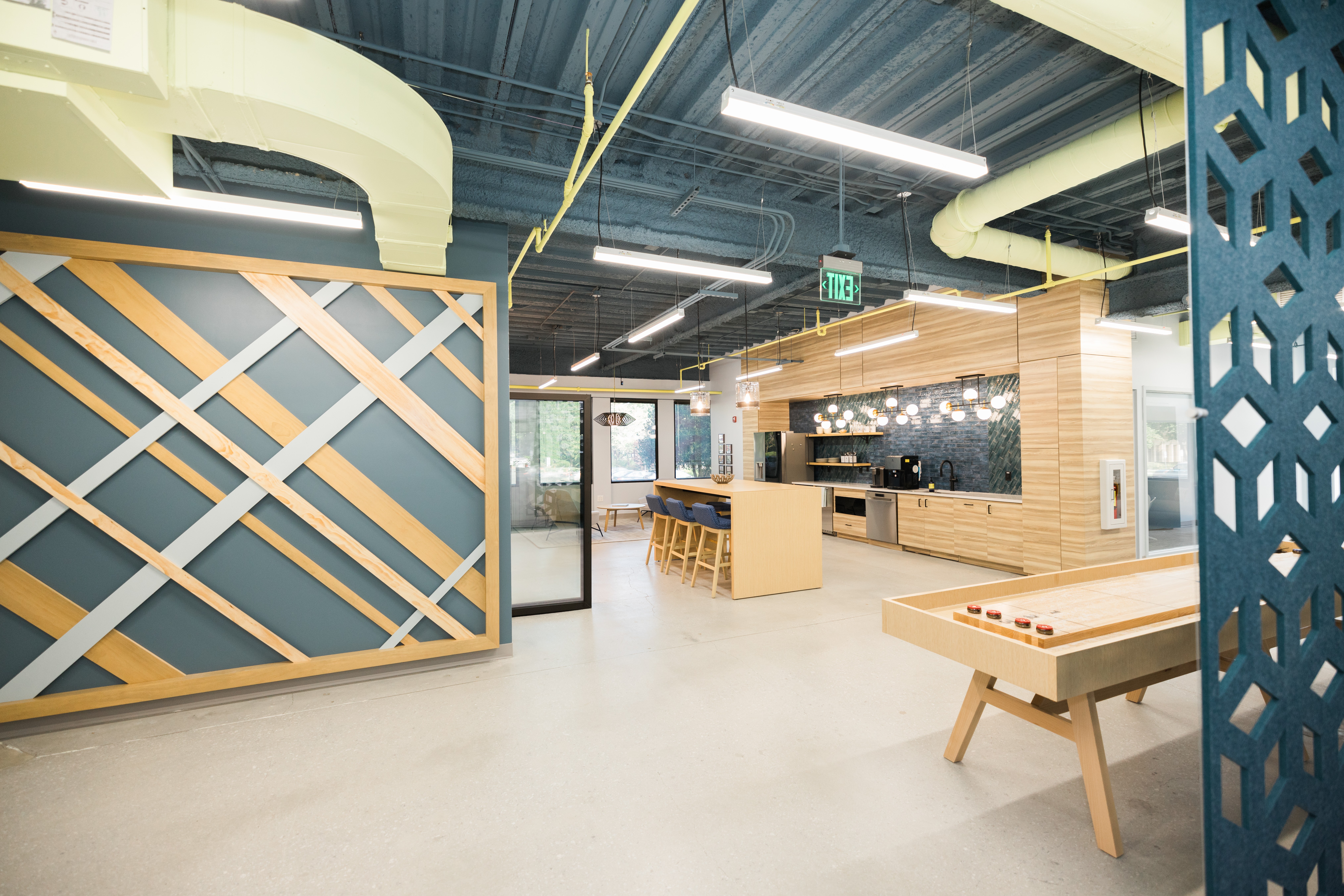 Indoor recreational space with game tables, seating, and modern decor, featuring bright lighting and industrial ceiling design.