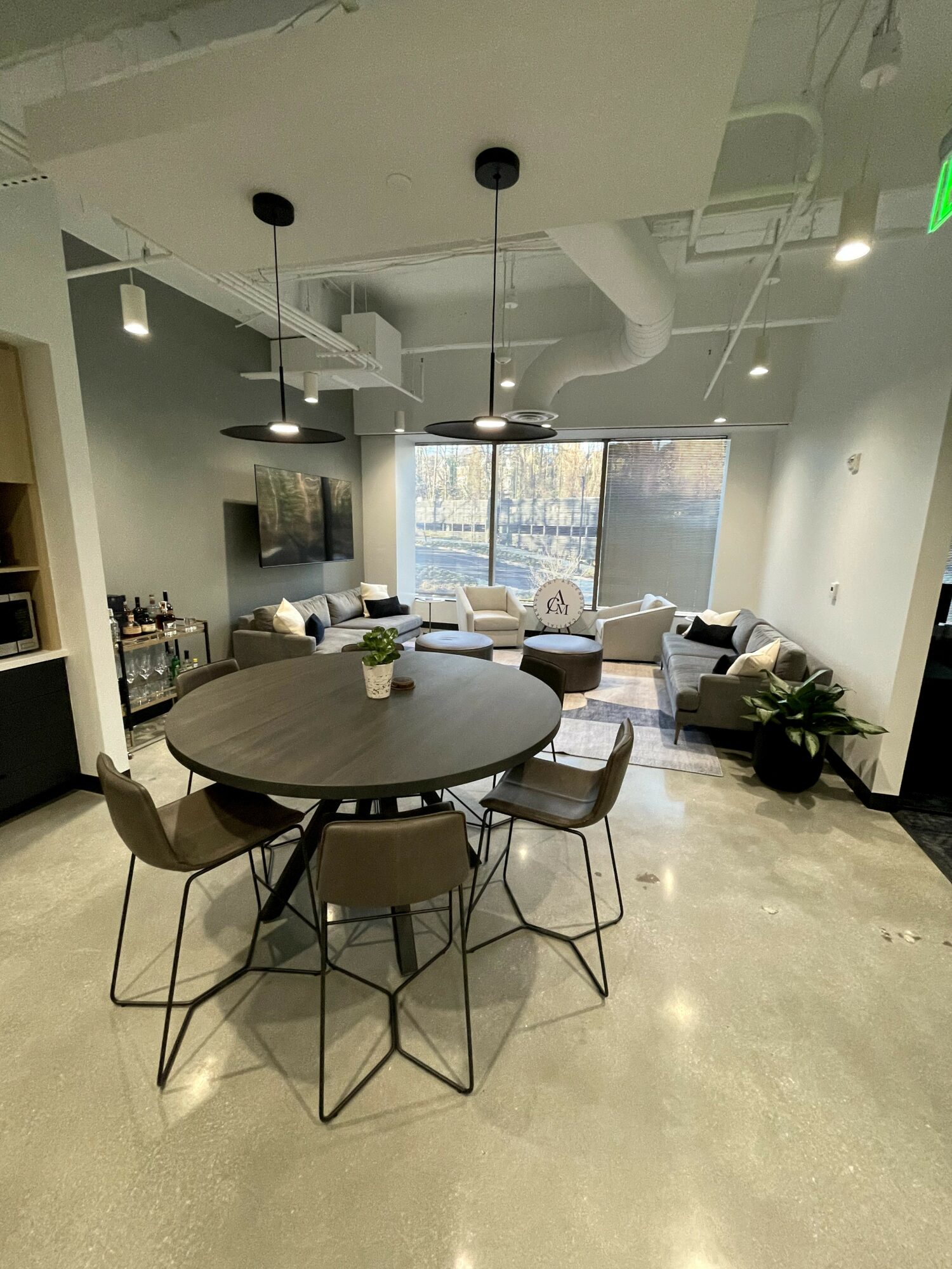 Modern lounge with round table, chairs, sofa, and large window, decorated with plants and artwork.