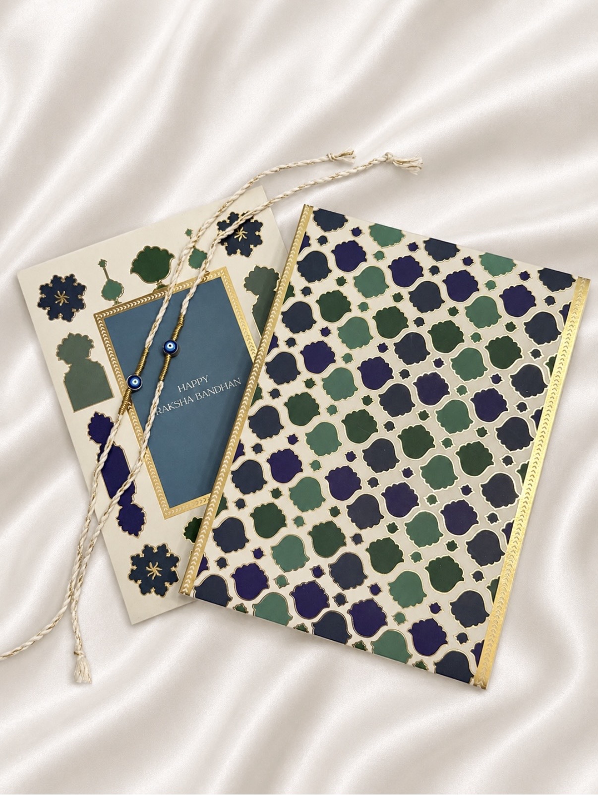 Two patterned notebooks with a string, one with a floral design and the other with a geometric pattern, on a satin surface.