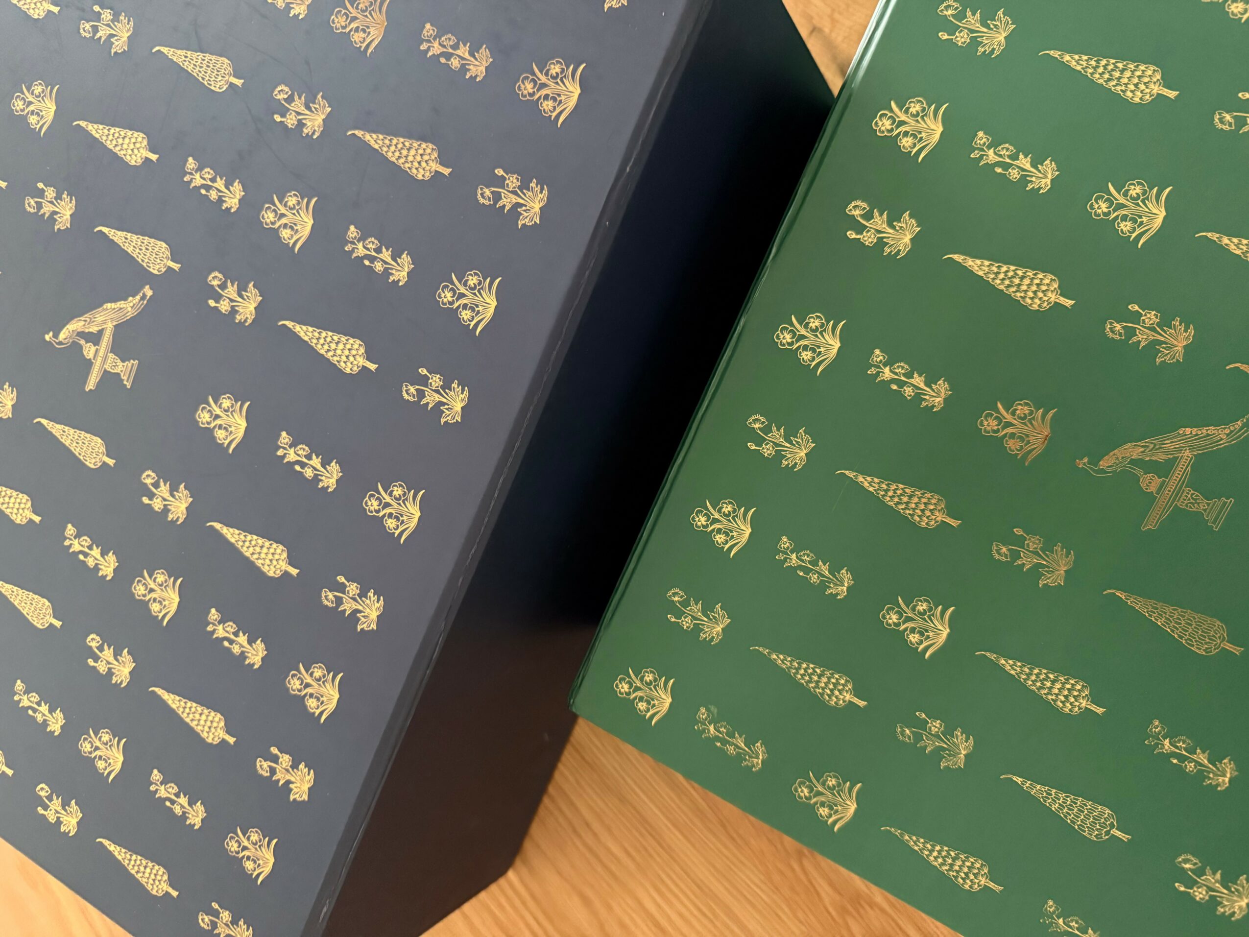Two books with gold embossed Christmas trees and ornaments on dark blue and green covers, placed on a wooden surface.