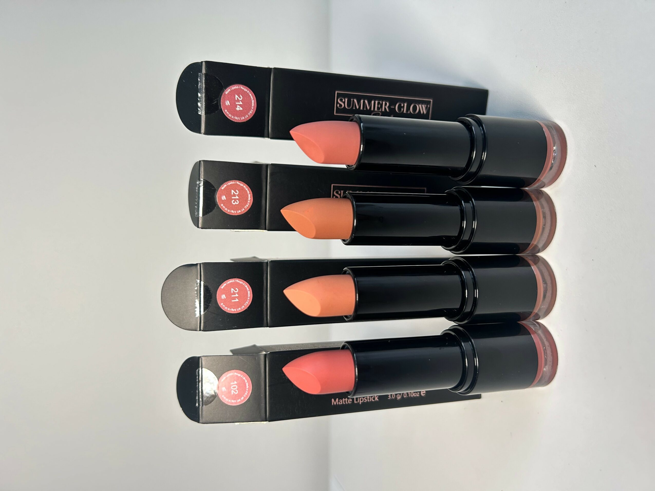 Four lipsticks in black tubes with pink shades, arranged horizontally on a white surface.