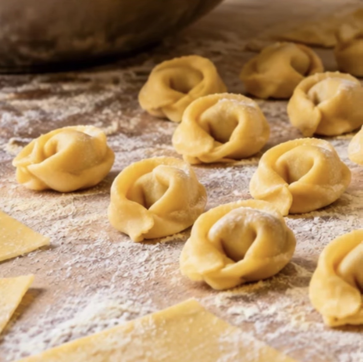 Dough tortellini arranged on a floured surface with a mixing bowl in the background.