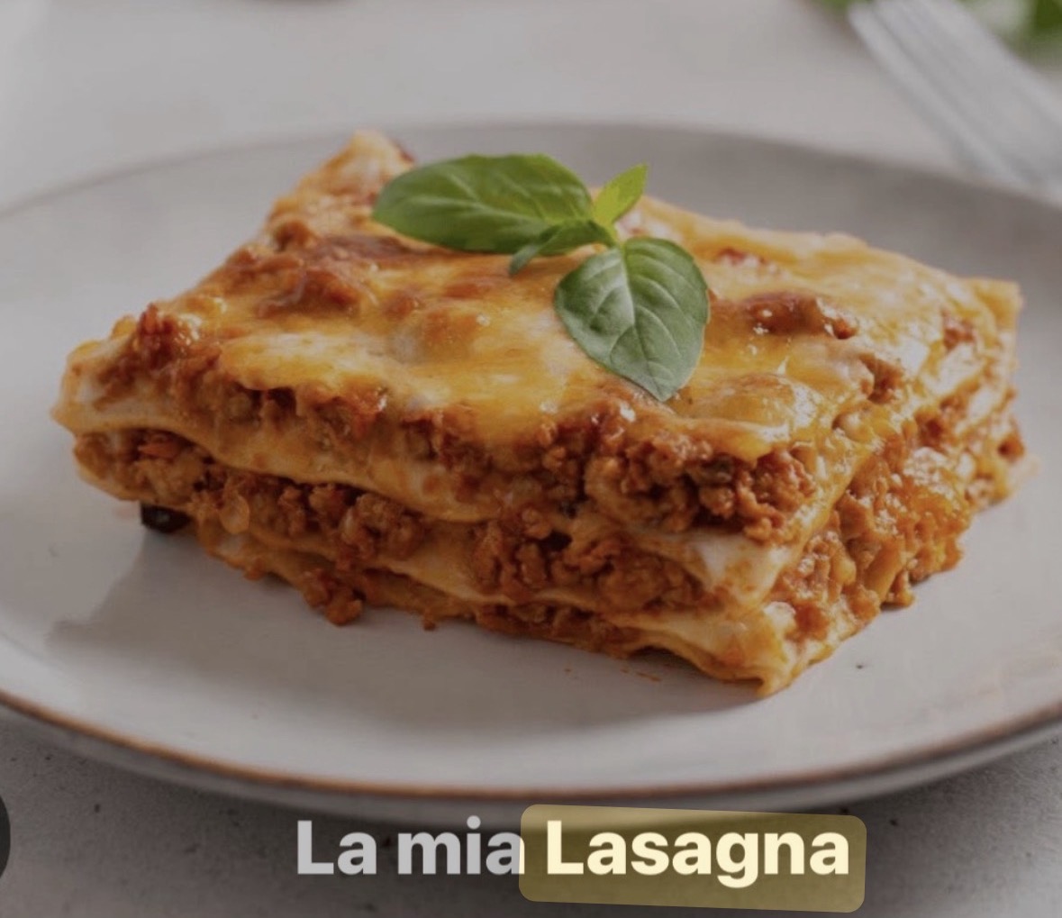 A serving of lasagna garnished with basil leaves on a white plate.