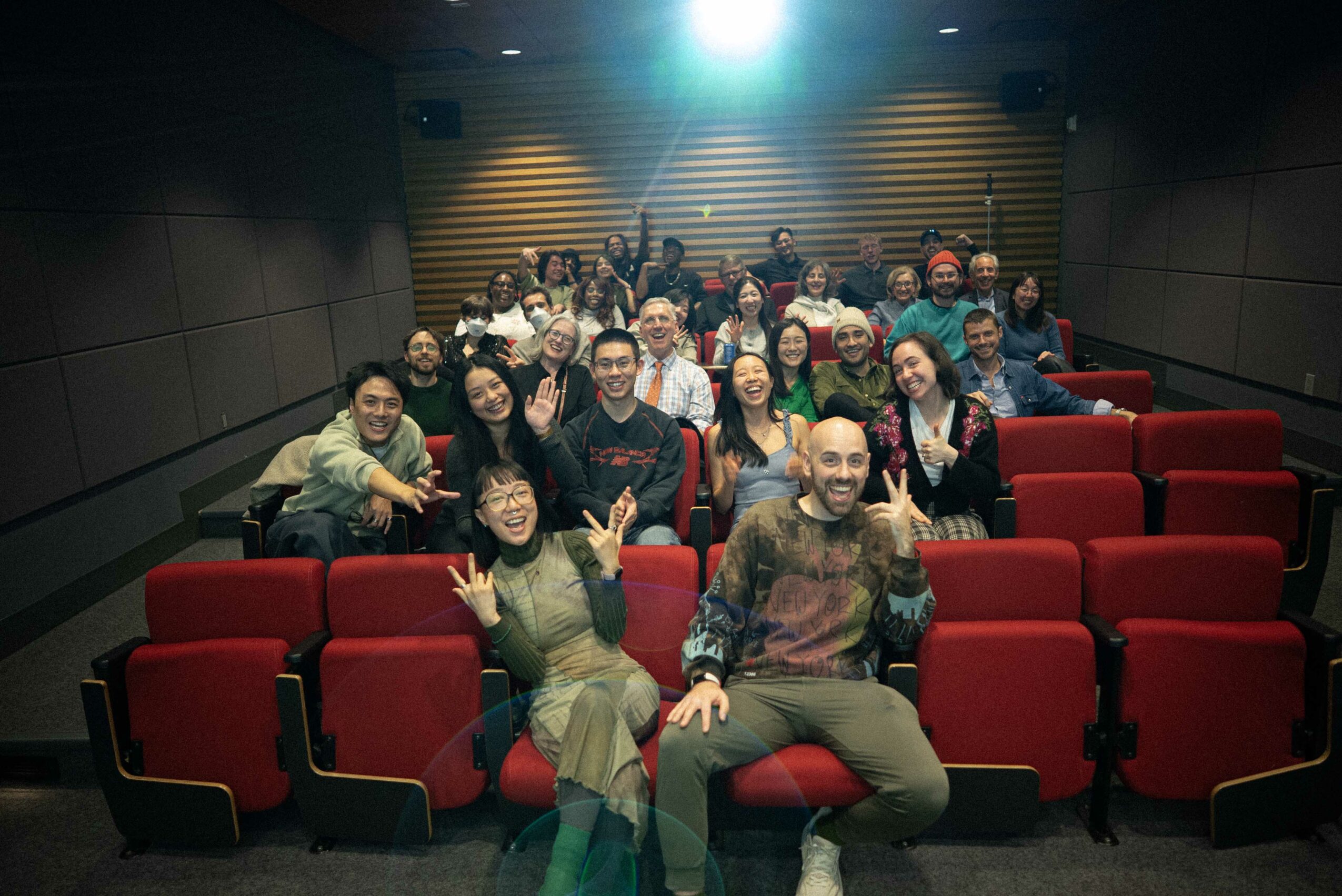 Group of people sitting in a theater with red seats, smiling and posing for the photo.