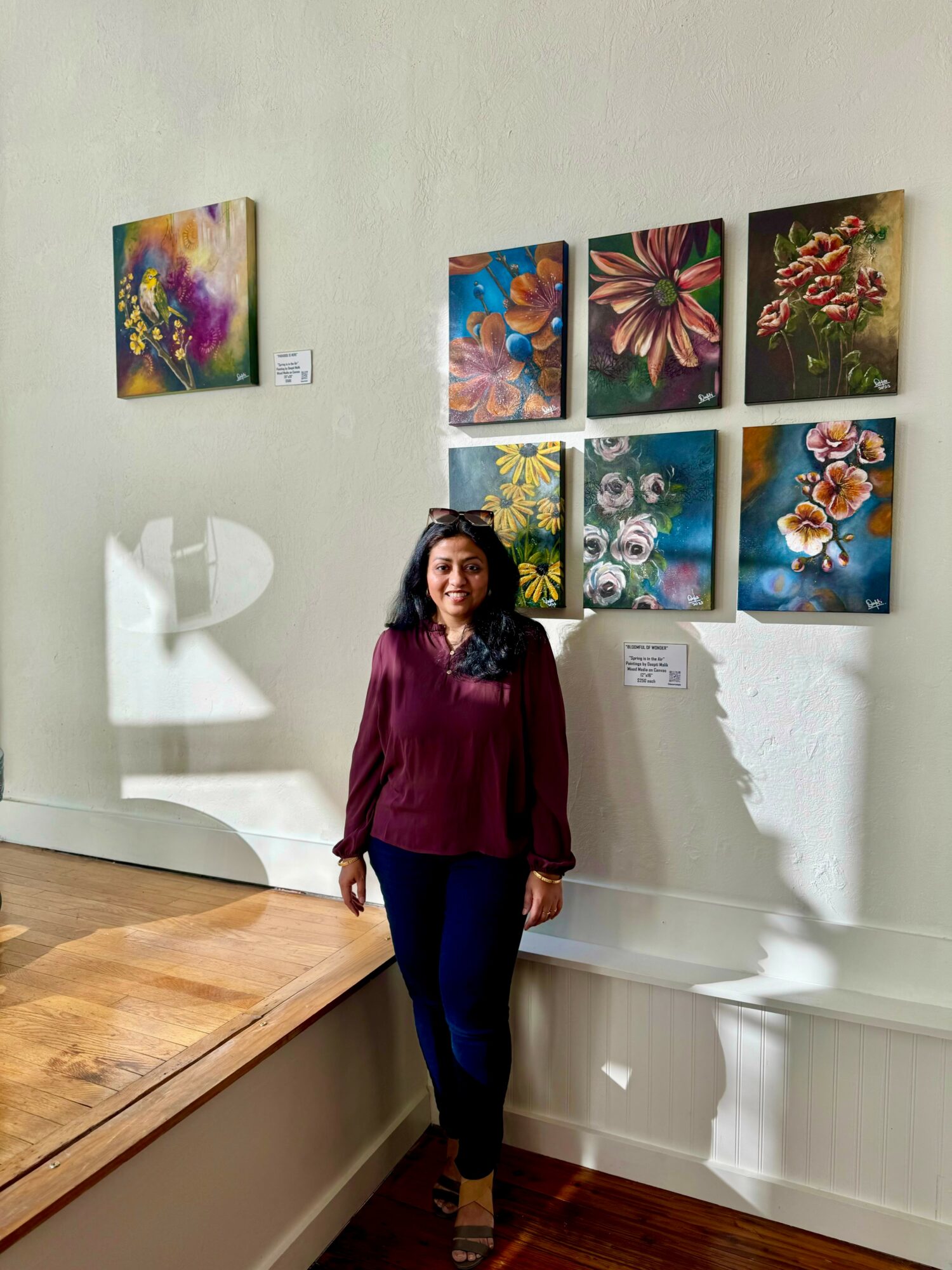 Woman standing in front of a wall with colorful floral paintings in an art gallery.