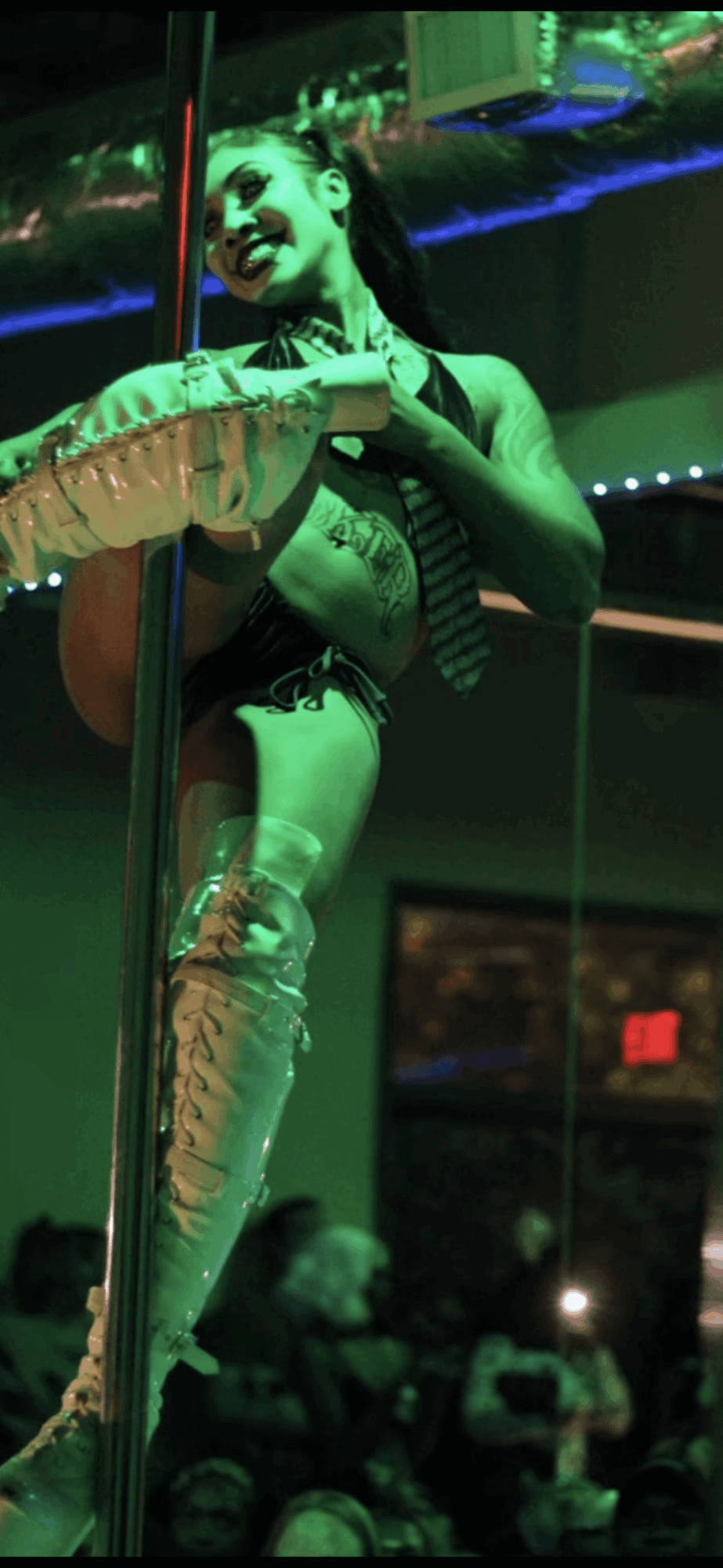 Circus performer balancing on a pole, wearing a costume with thigh-high boots, in front of an audience.