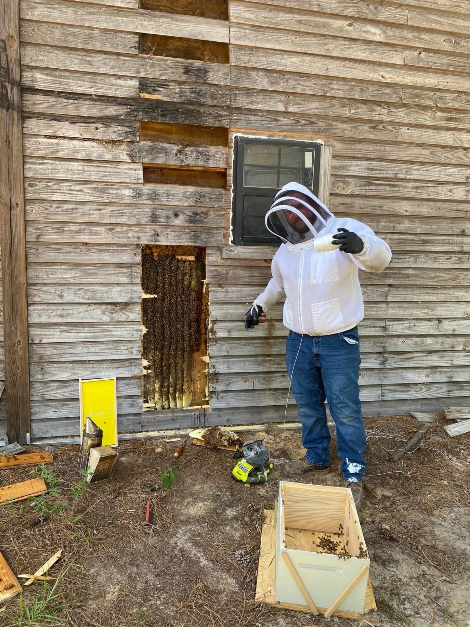 Child in protective gear working outside a wooden wall with a small window, surrounded by tools and materials.
