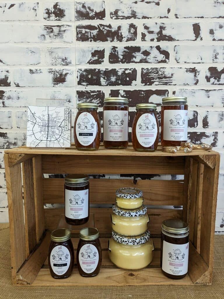 Wooden crate with jars of honey and a stack of honeycomb, against a brick wall background.