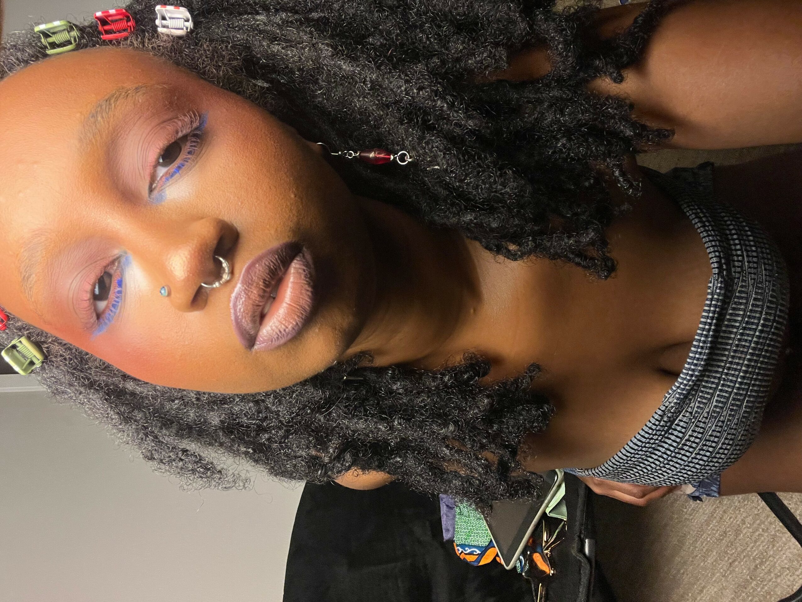 Close-up of a person with styled hair, makeup, and jewelry, looking at the camera.