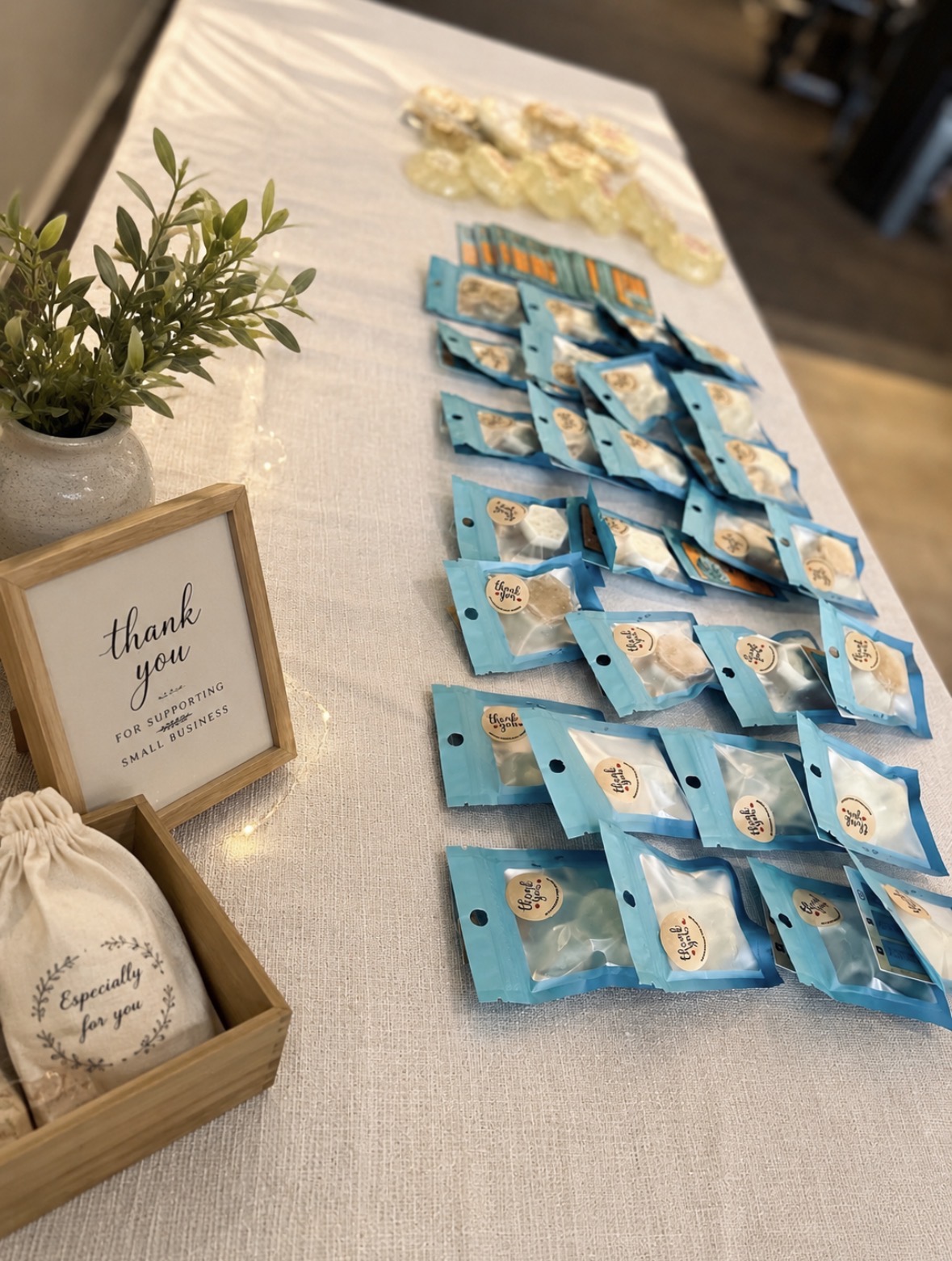 Table with blue packaged items, a small plant, and a framed thank you note, viewed from the side.
