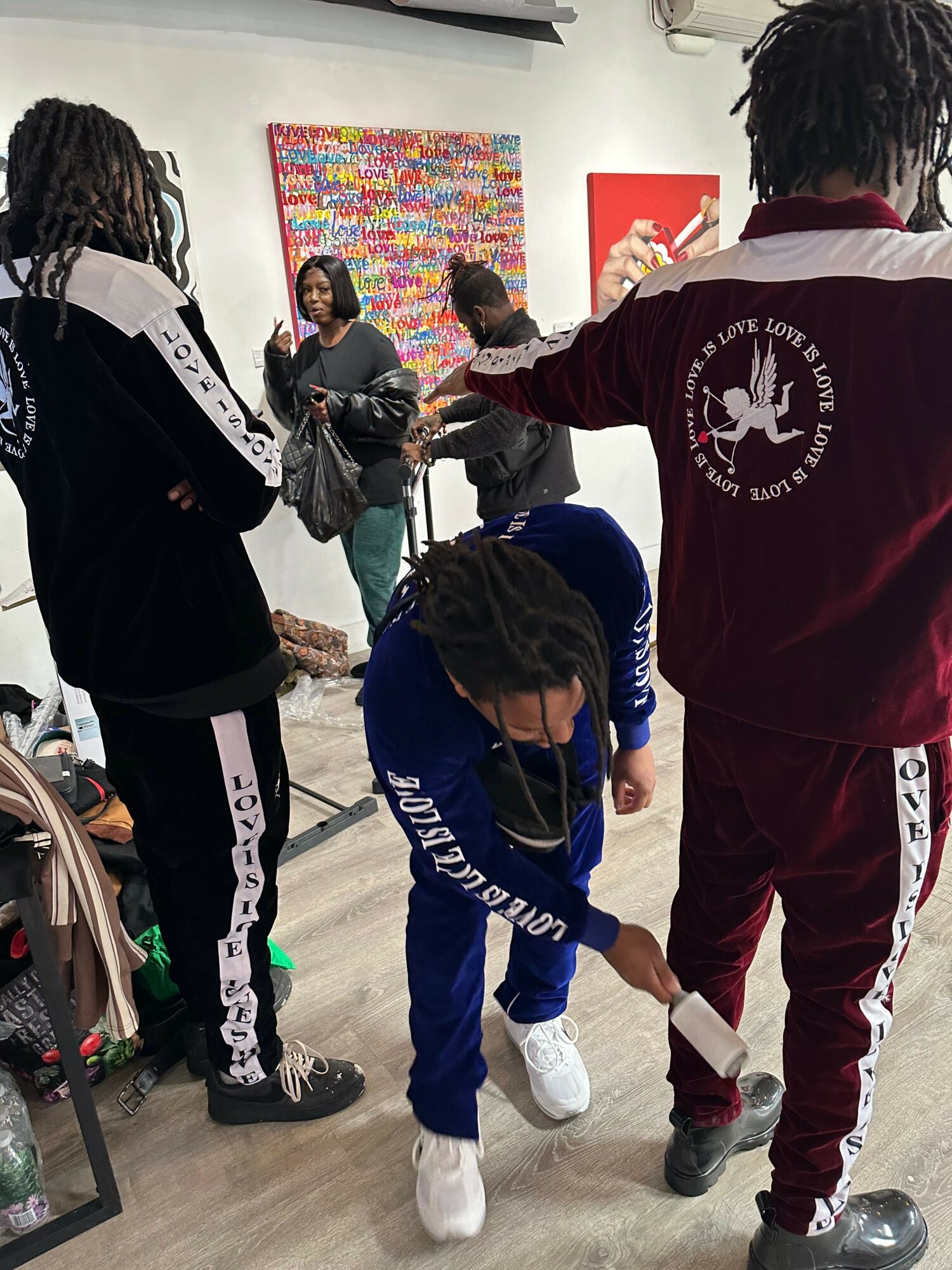 Three people in casual clothing, one holding a microphone, standing in an indoor space with colorful artwork on the wall.